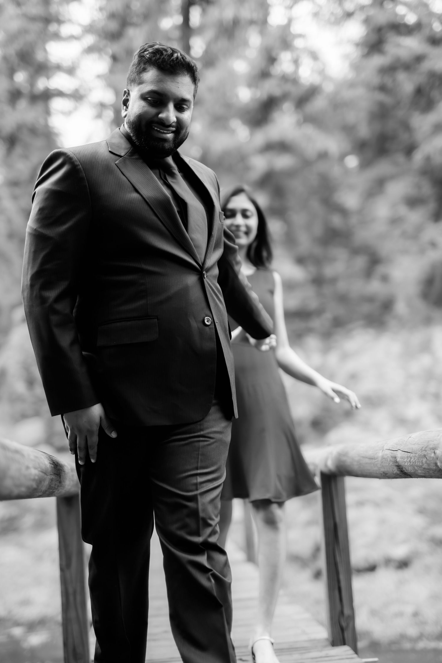 Black and white portrait of couple in formal wear posing on wooden bridge.