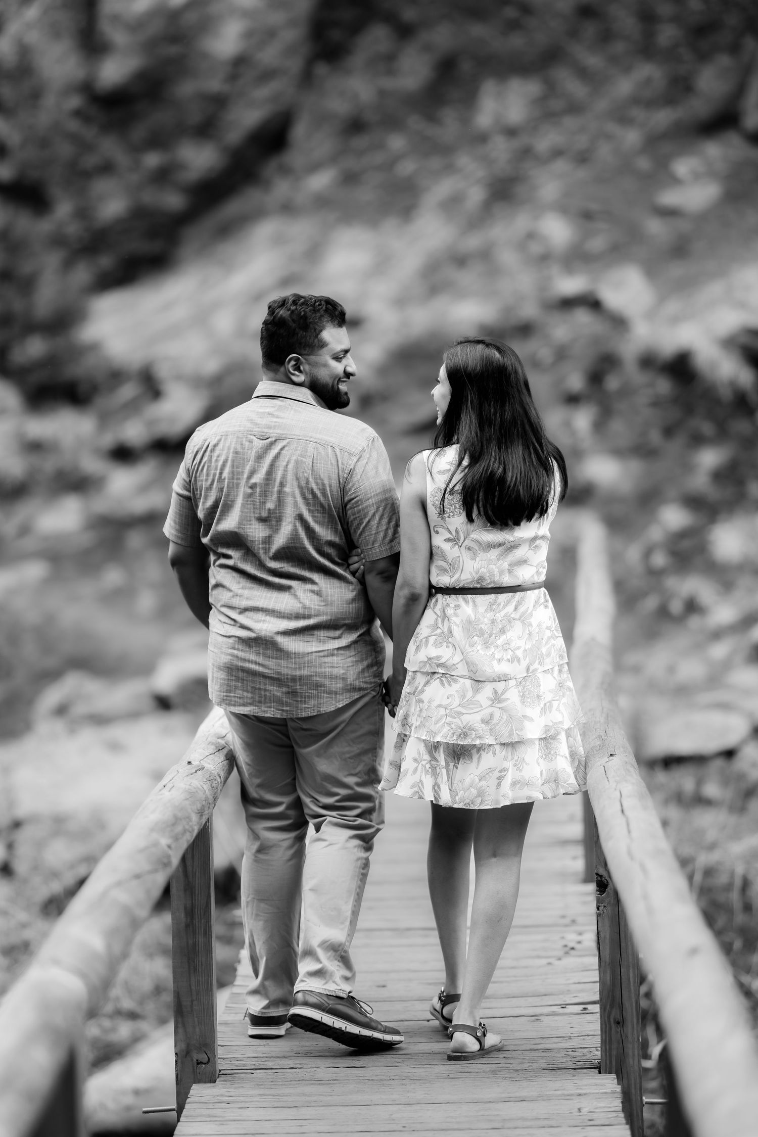 A couple walking hand in hand on a wooden footbridge surrounded by nature in monochrome.