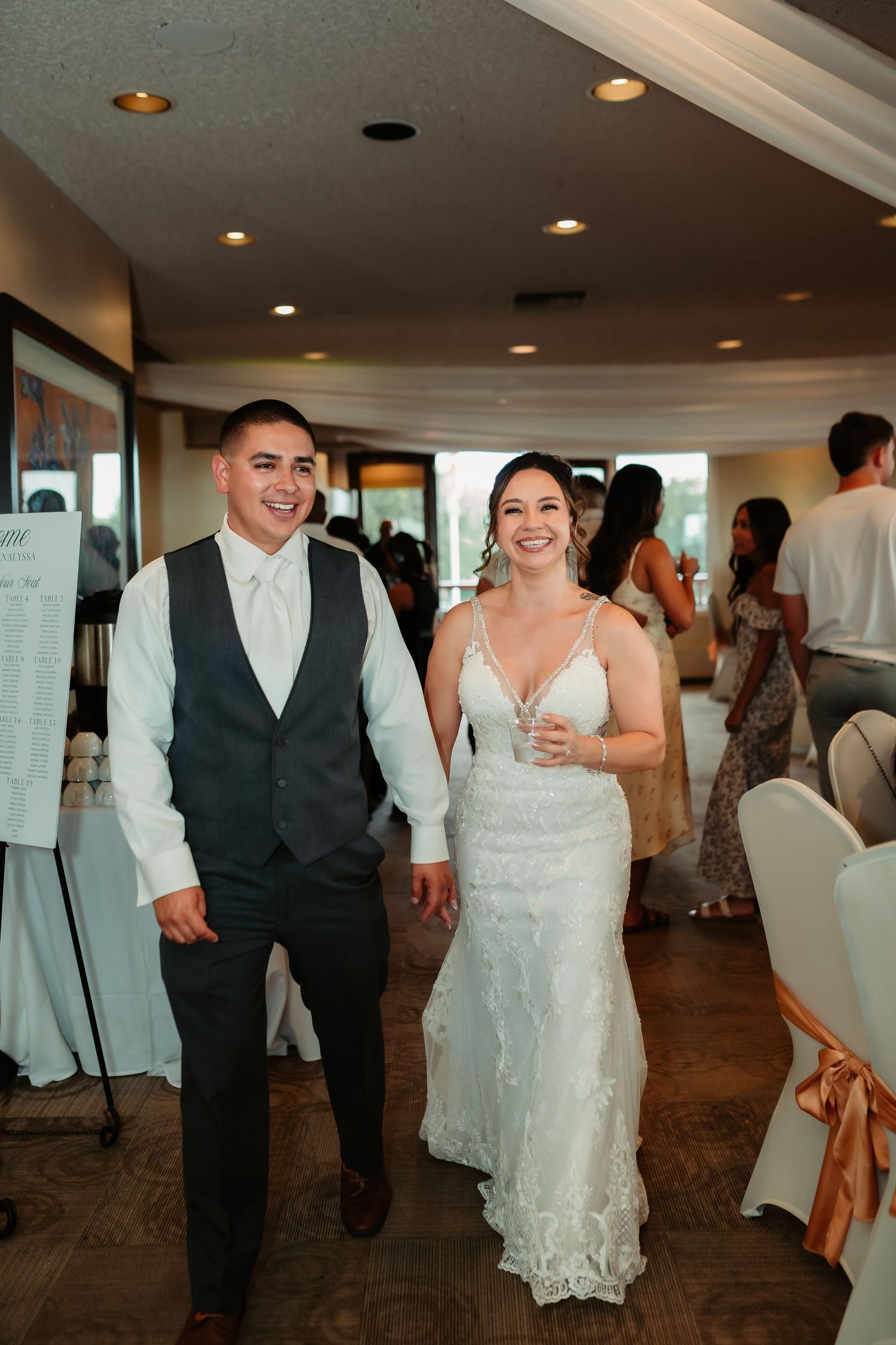 A wedding couple walks together in formal attire through an elegantly lit reception venue.