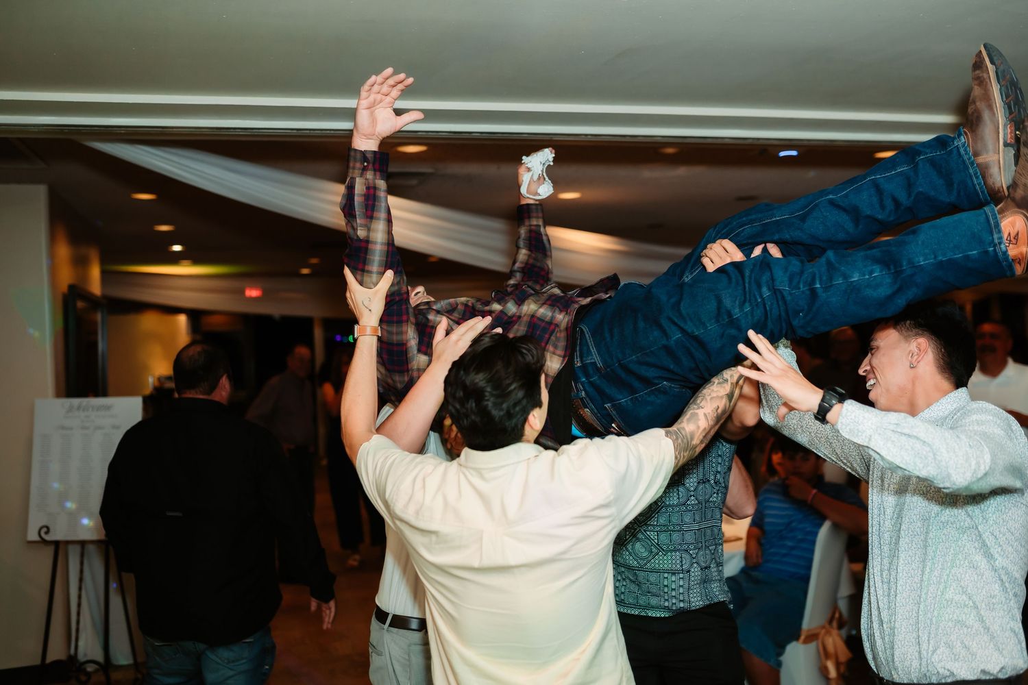 Wedding guests dancing energetically with raised arms on reception dance floor.