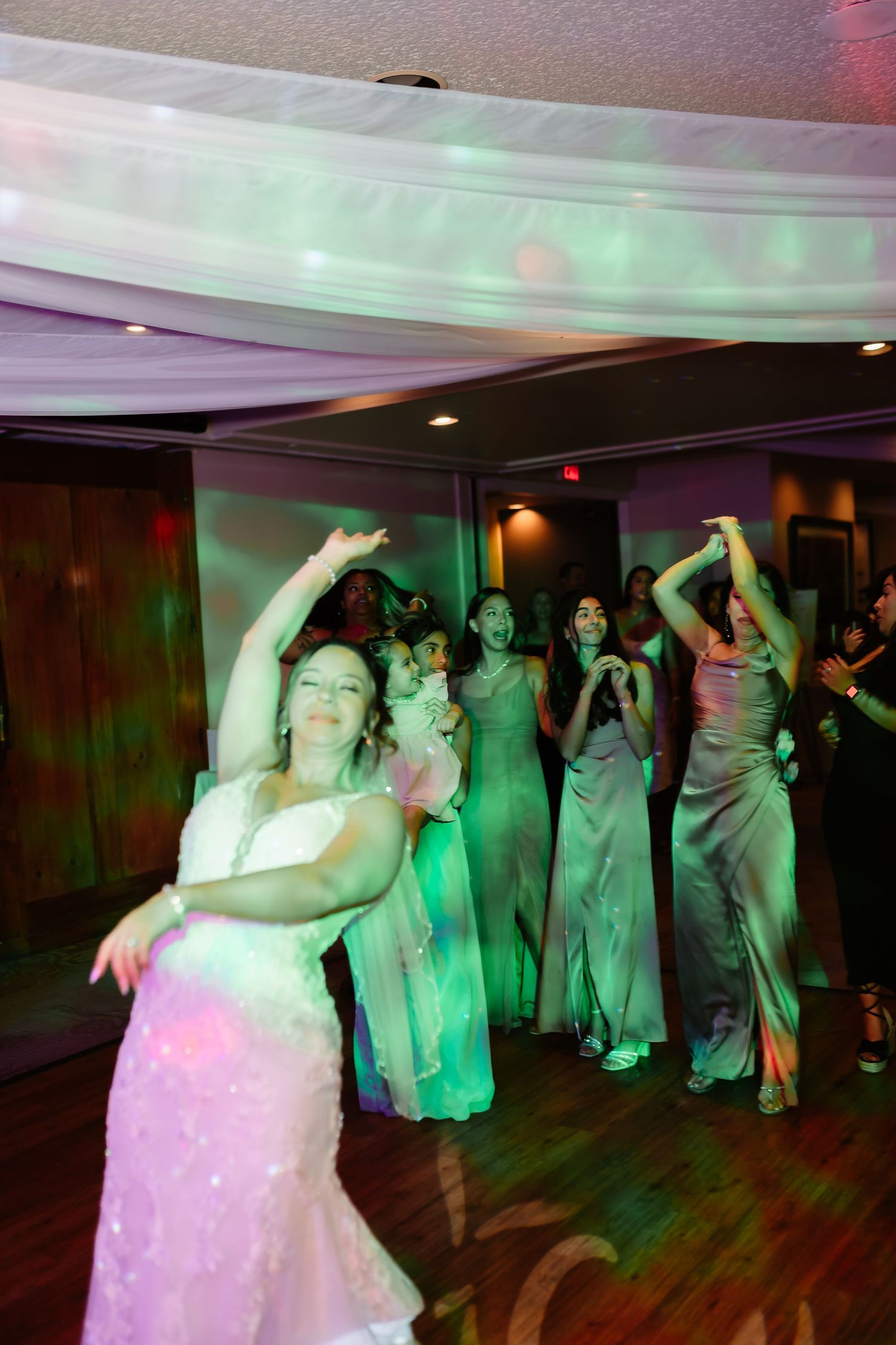 Wedding guests dancing under colorful lights at a reception with a white draped ceiling.