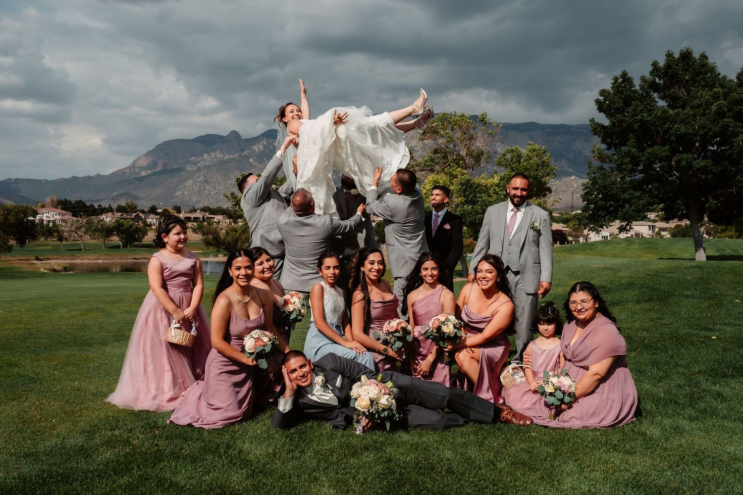 Wedding celebration under dramatic mountain landscape with wedding party in pink dresses enjoying candid moments in nature.