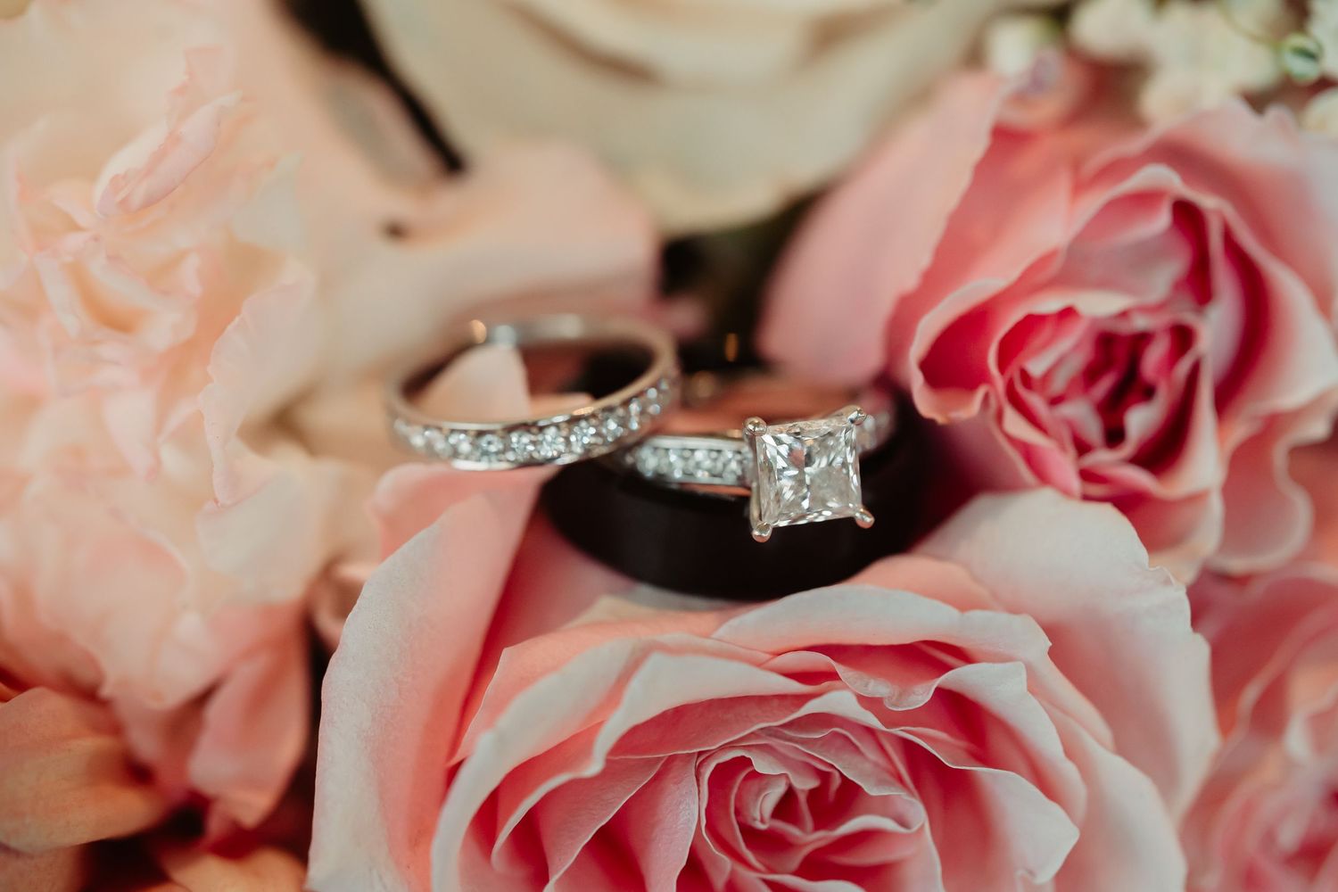 Close up detail of delicate pink and white roses with sparkly diamond wedding rings nestled among the petals.