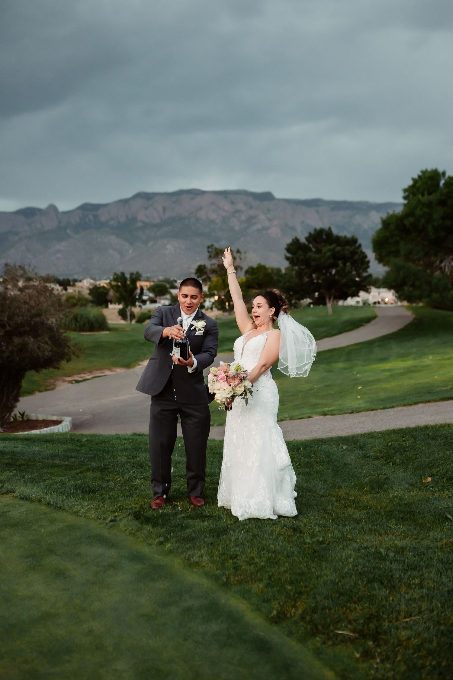 A wedding couple shares a joyful moment on a golf course with mountains in the background.