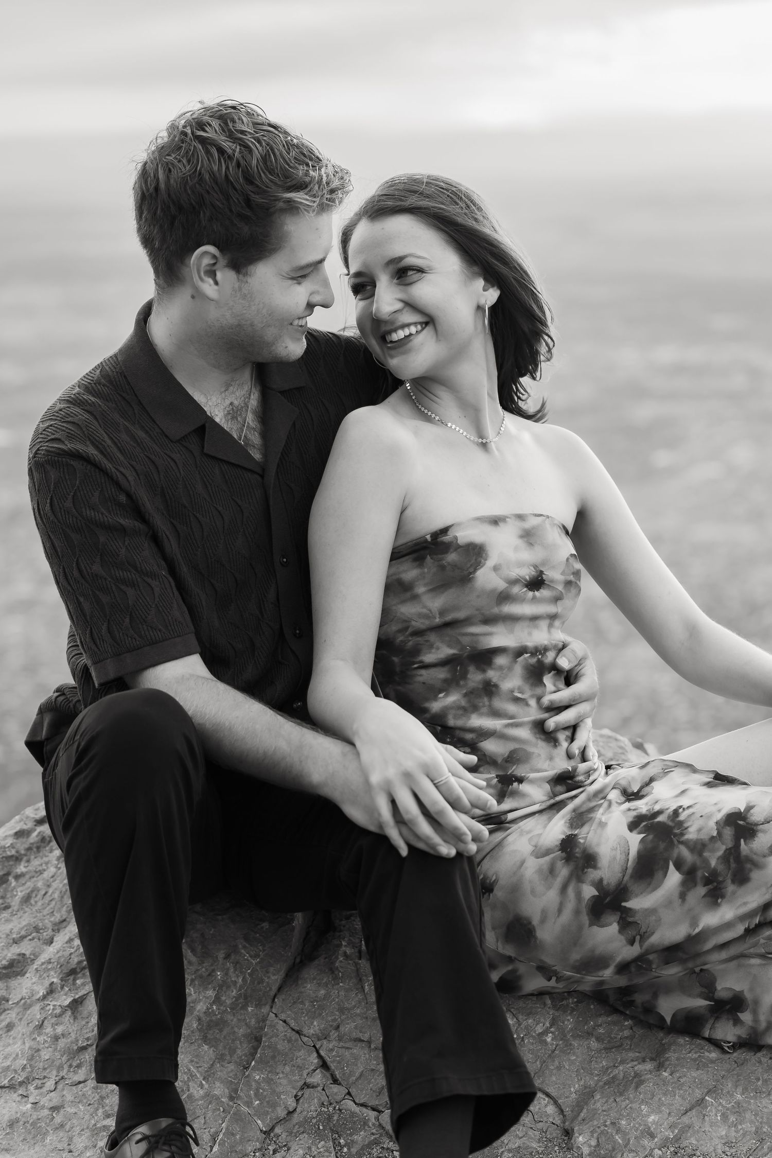 A black and white engagement photo captured on a dramatic mountain ledge.