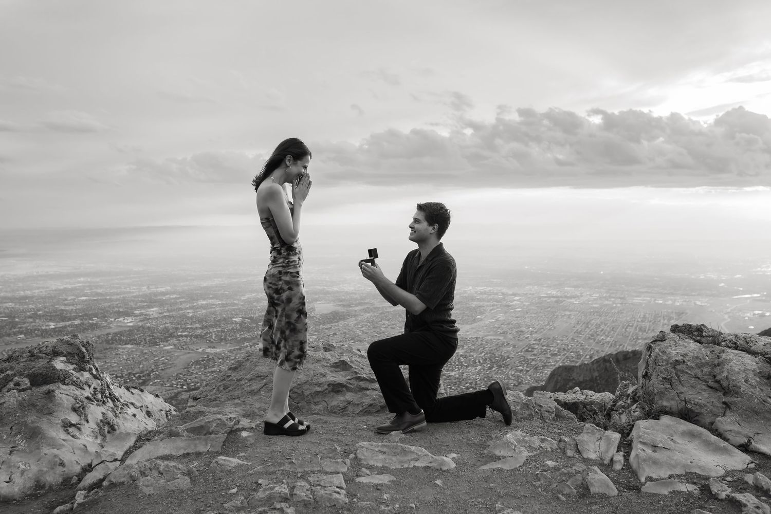 A proposal scene unfolds across scenic mountain views as a couple celebrates their engagement at sunset.
