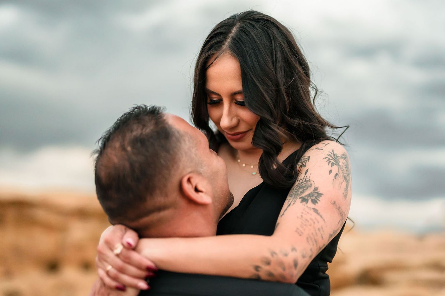 Woman with tattoos smiling while embracing man during desert engagement photography session.