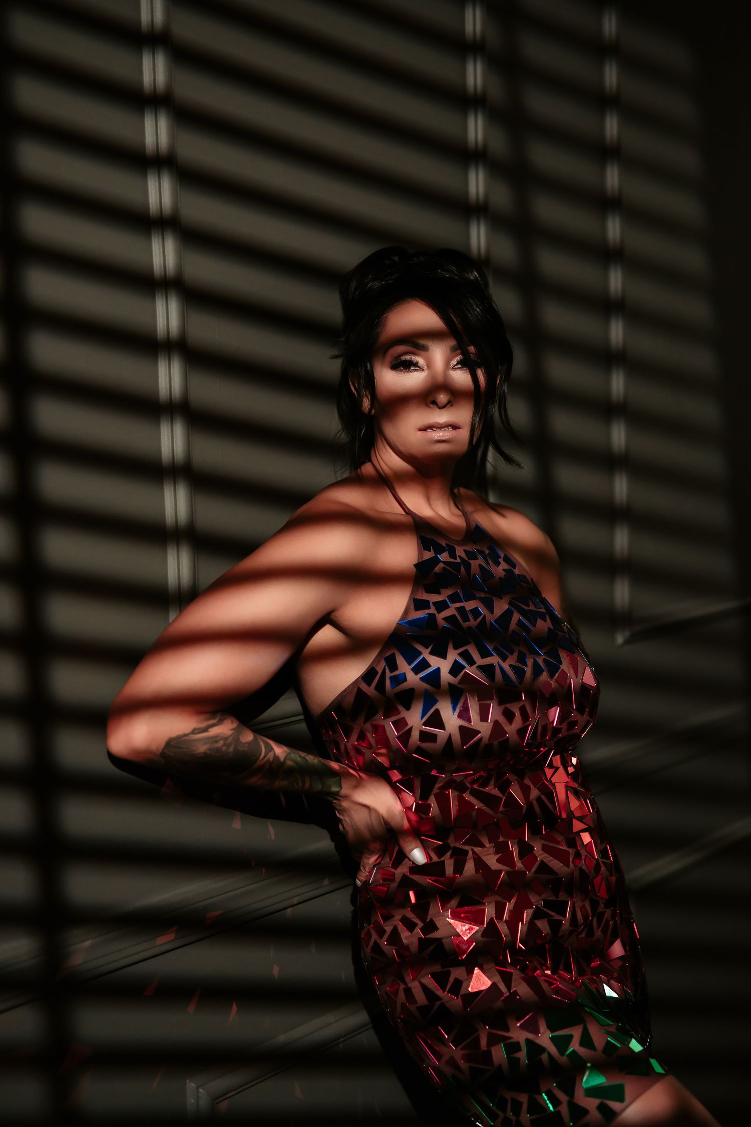 Dramatic fashion portrait showing a figure in a red textured dress posing against venetian blind shadows.
