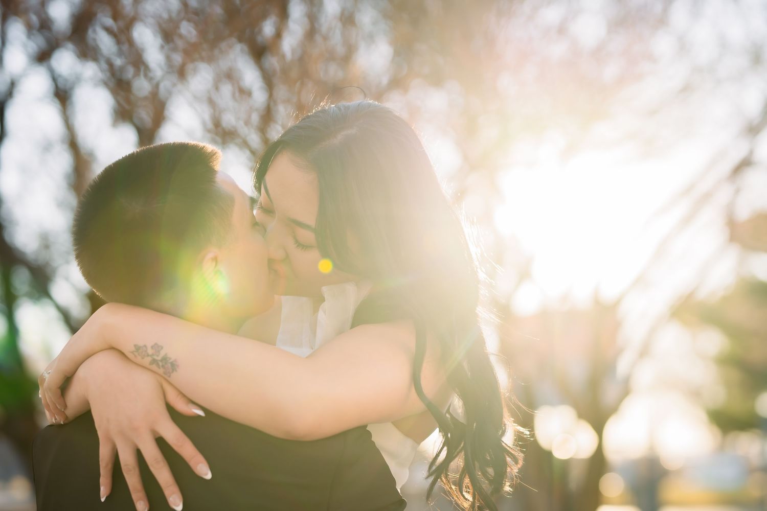 Silhouetted hands reach towards bright sunlight filtering through trees creating a dreamy backlit effect.