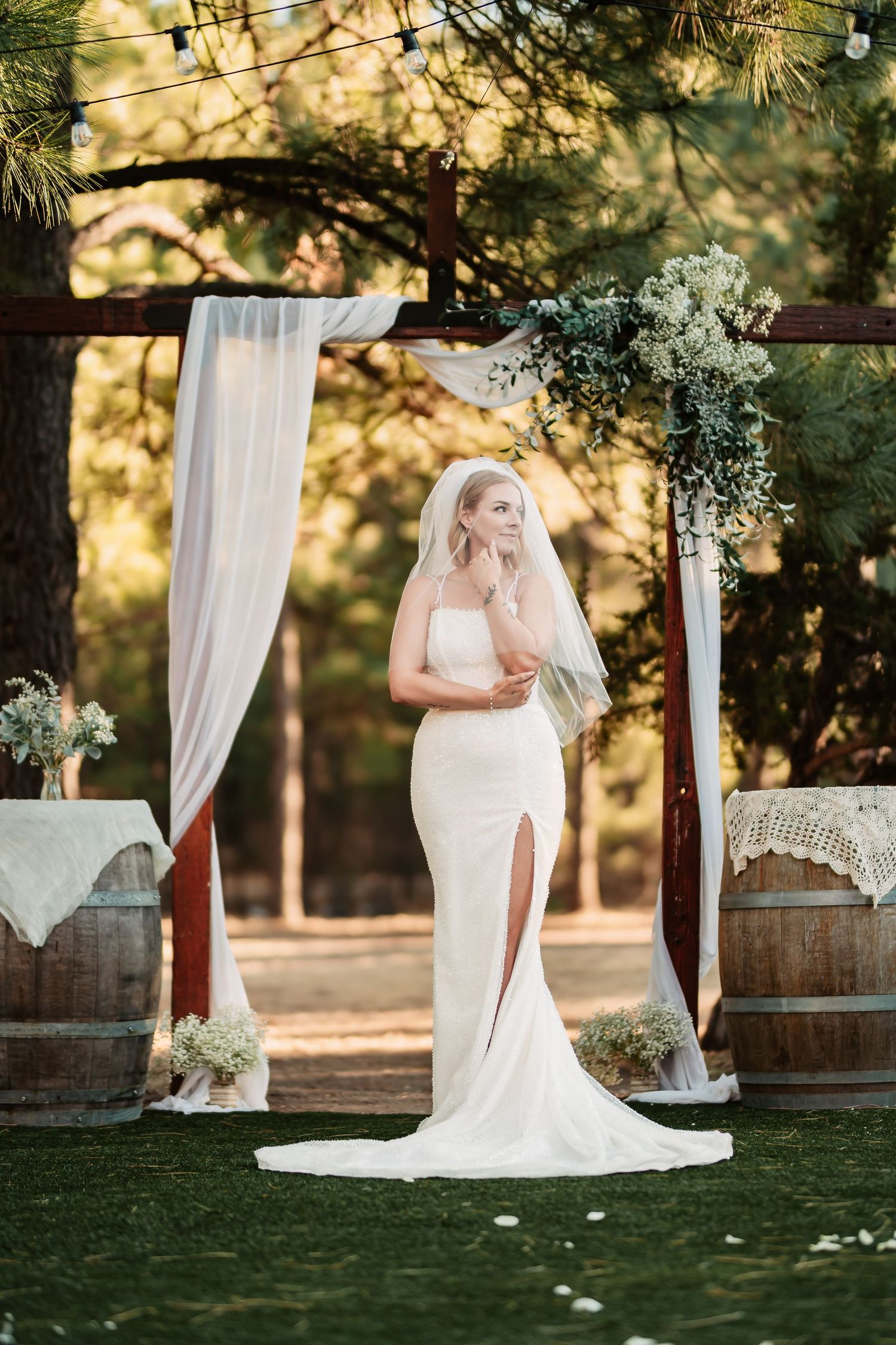 An elegant outdoor wedding ceremony setup with white drapes and barrels against a rustic woodland backdrop.