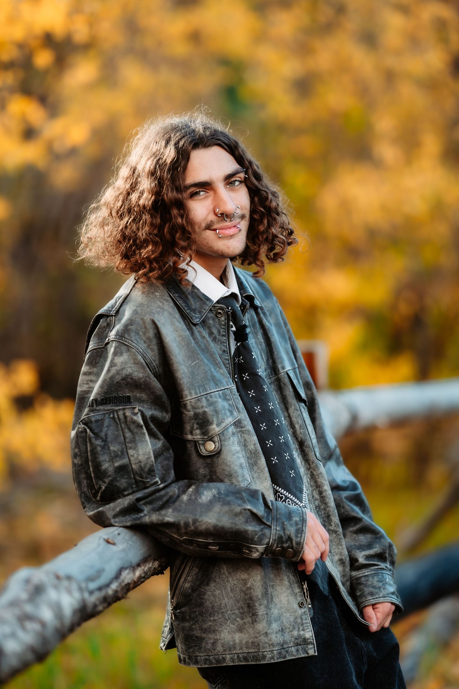 A person in a denim jacket poses outdoors against a warm autumn background with golden foliage.