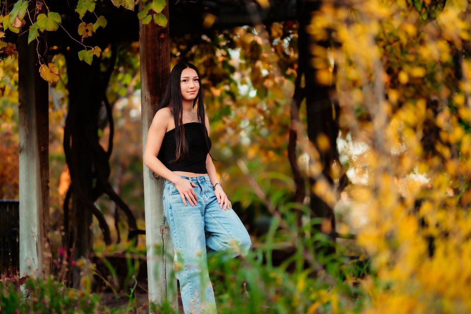 Woman in a blue dress poses gracefully among vibrant autumn foliage in a natural outdoor setting.