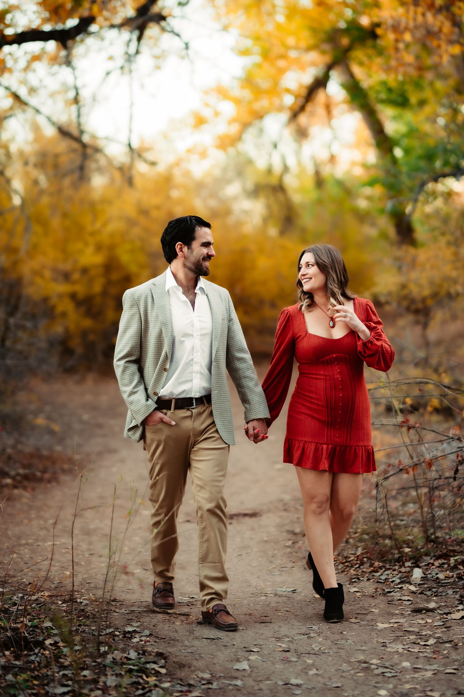 A couple walks hand in hand through a scenic autumn forest path with golden foliage in the background.