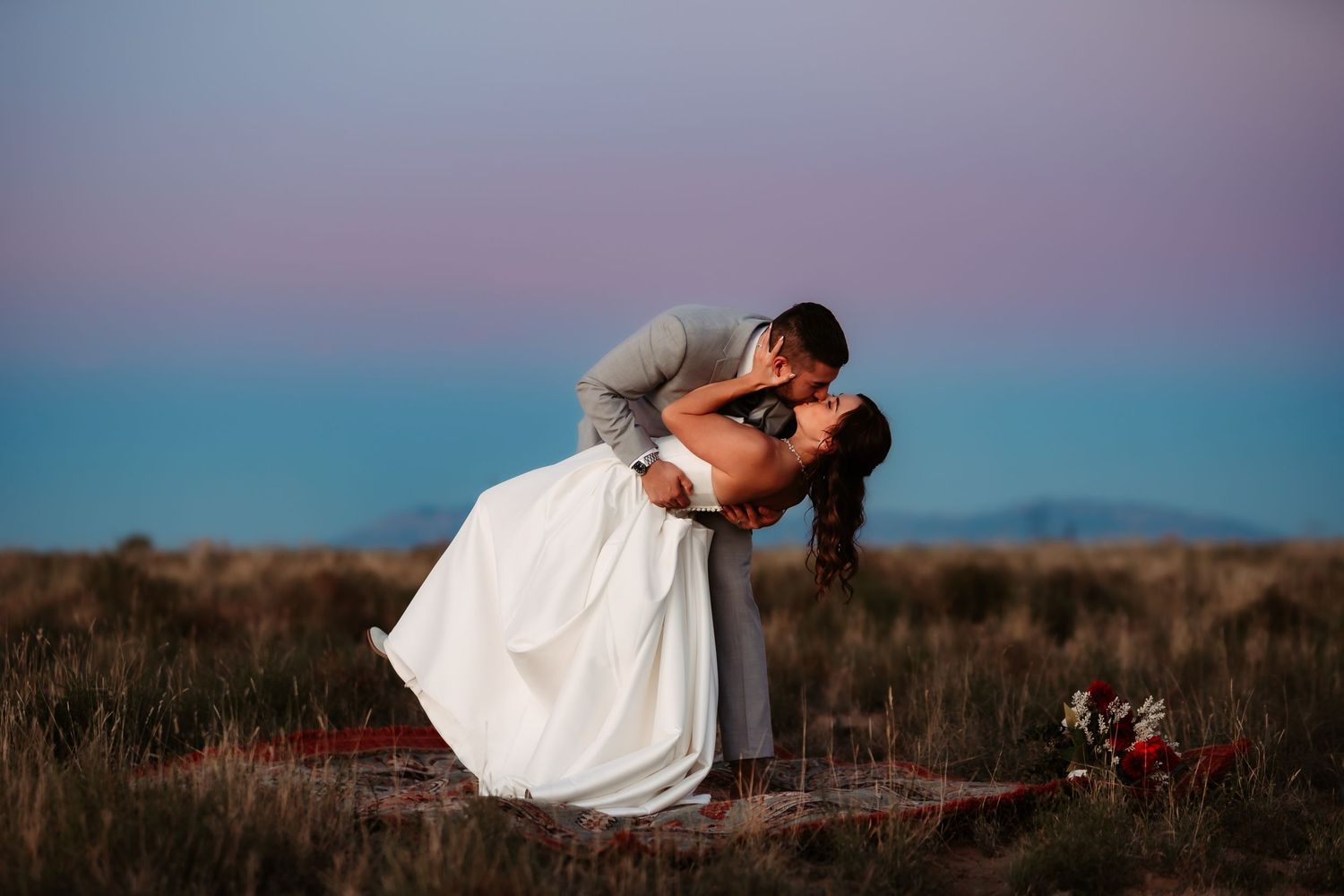 Silhouettes of a couple kissing during sunset in a romantic outdoor wedding photo shoot.