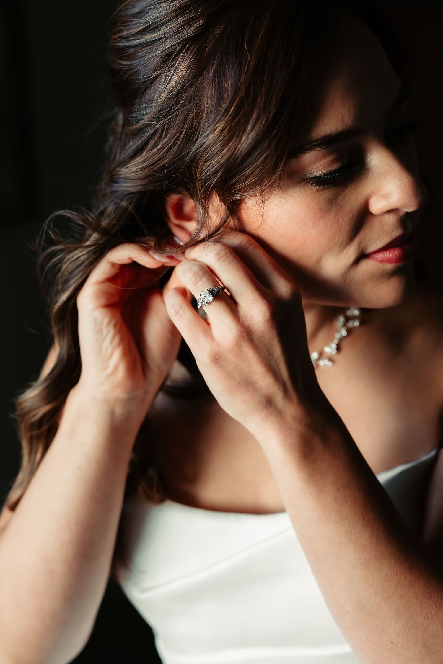 A sequence of close-up shots showing hands putting on an elegant earring in soft, dramatic lighting.