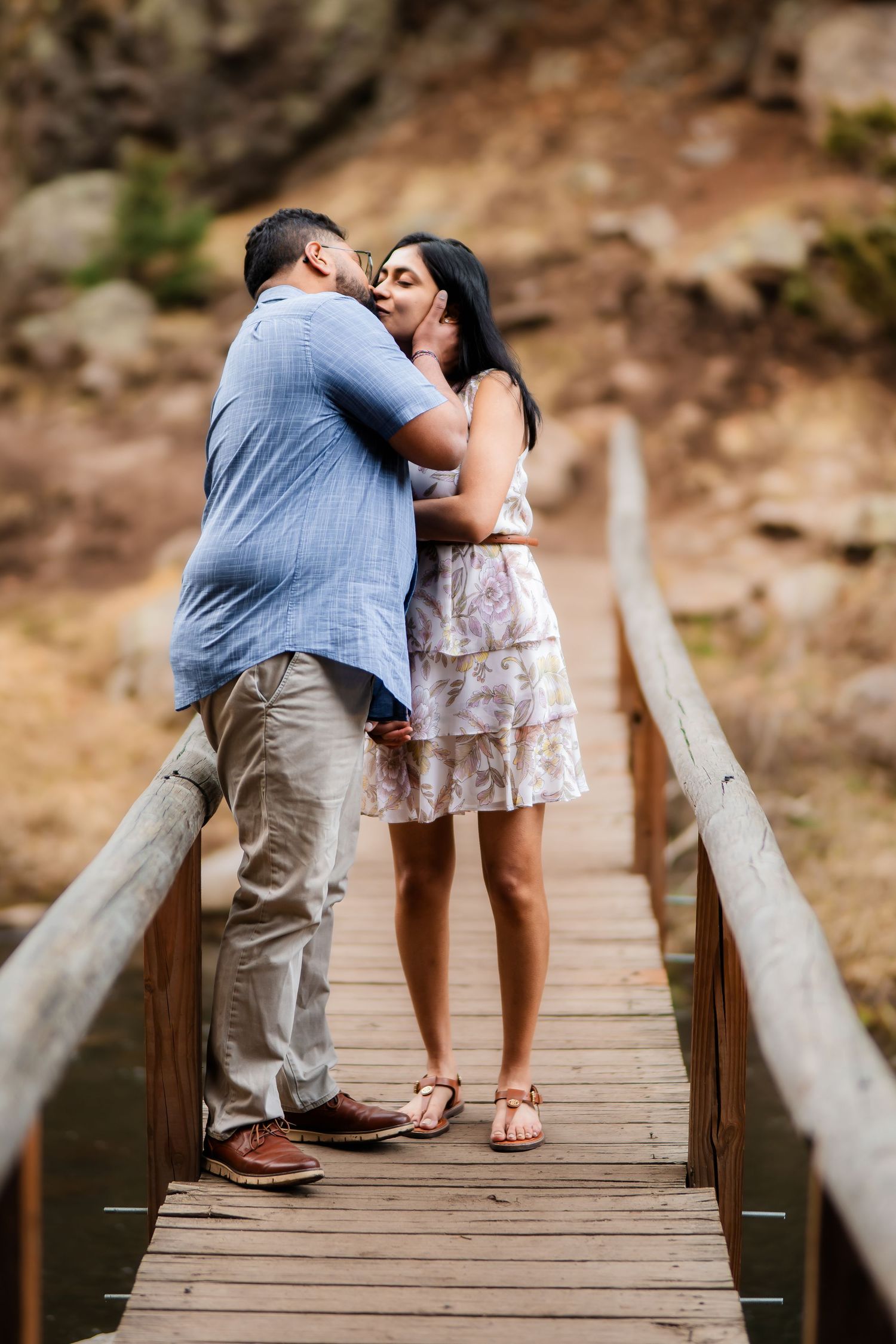 A romantic moment shared between a couple on a wooden bridge in nature.
