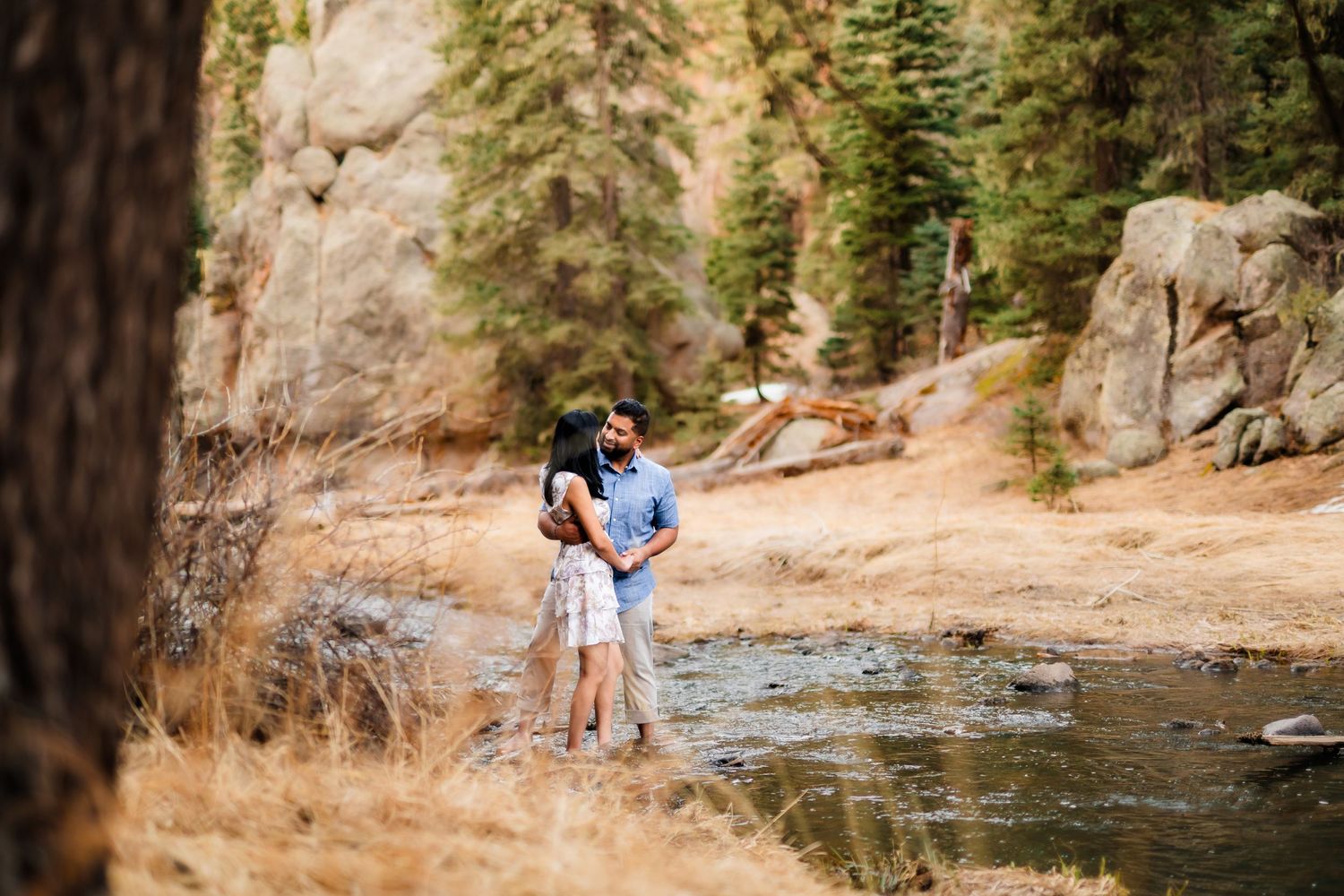 A couple poses together near a scenic mountain stream during a romantic outdoor photoshoot.
