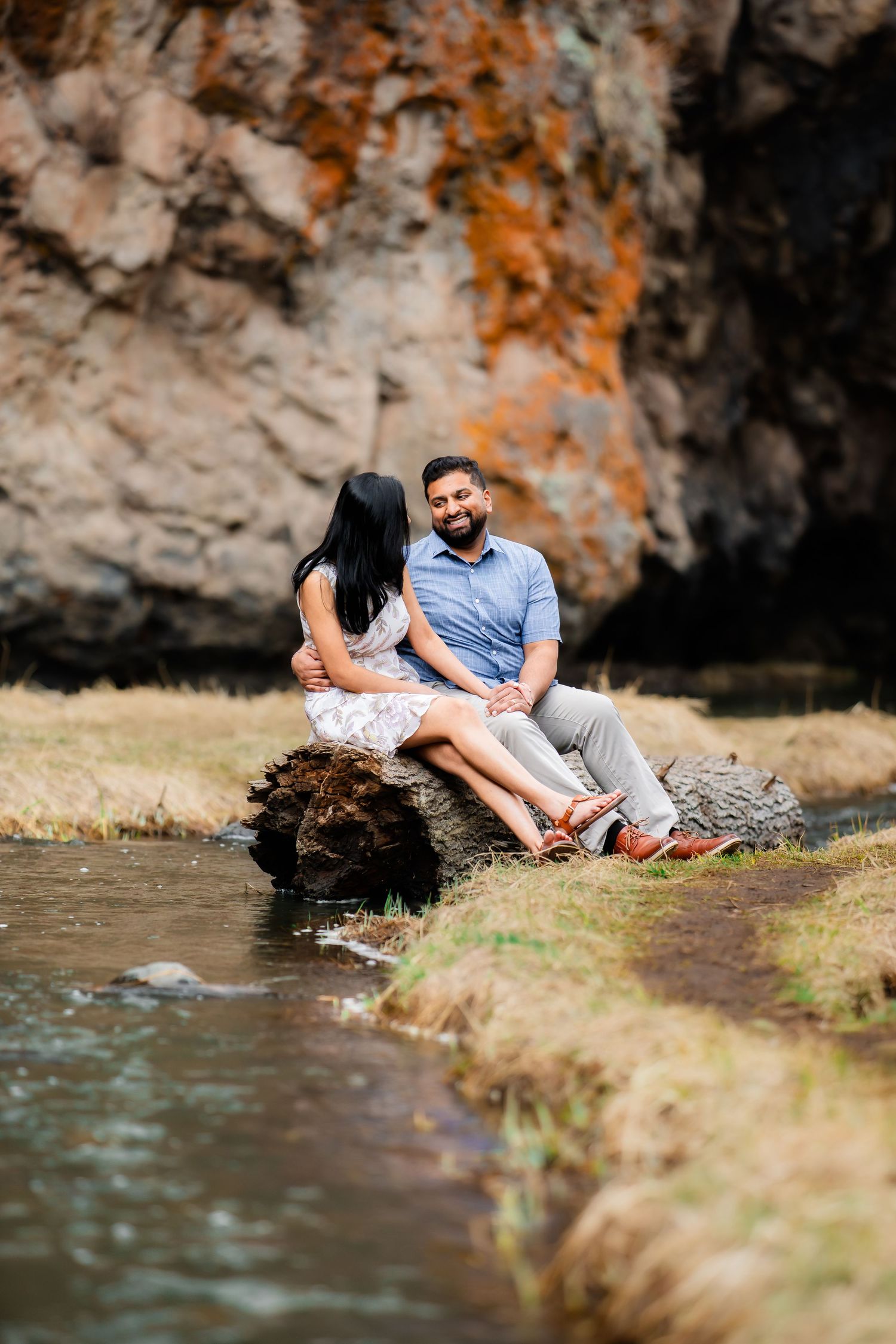 A romantic photoshoot by a stream with rocky cliffs in the background.