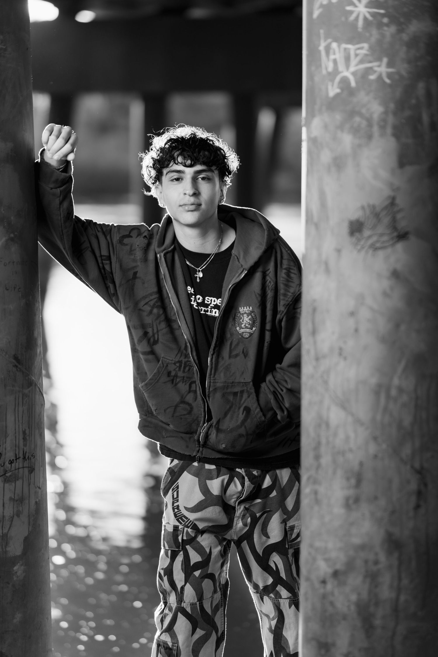 Black and white portrait of someone posing by concrete pillars in an urban setting.