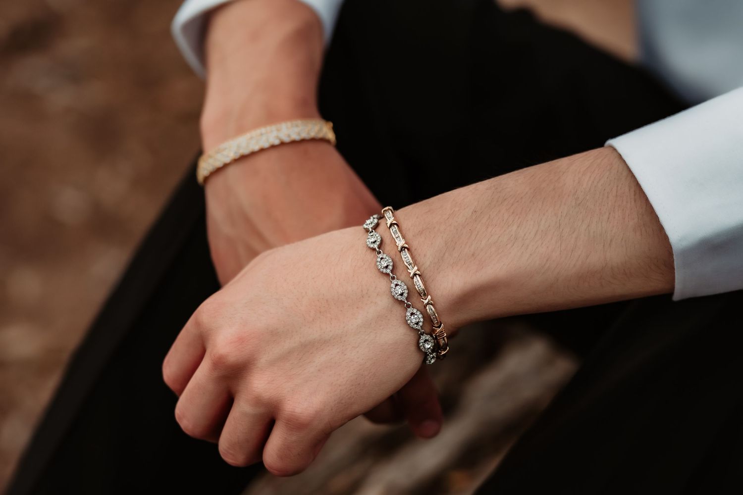 Close-up of hands wearing delicate silver bracelets against dark fabric background.