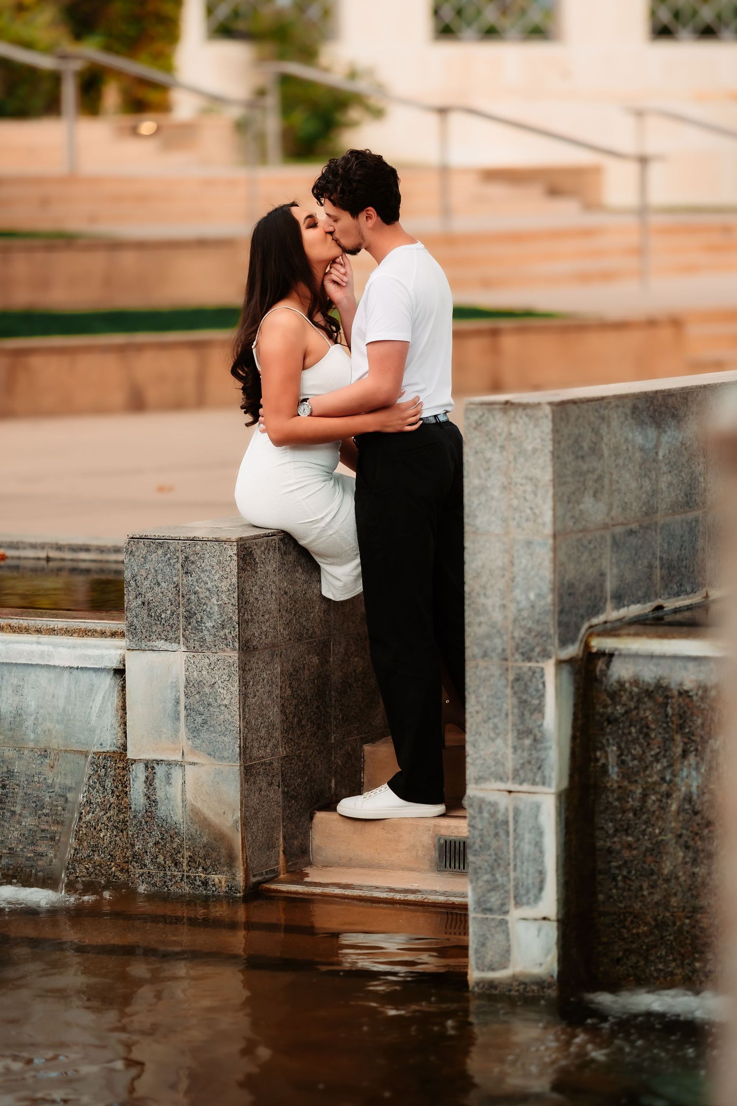 A romantic couple sits on stone steps near a water feature at sunset, creating an intimate series of moments.