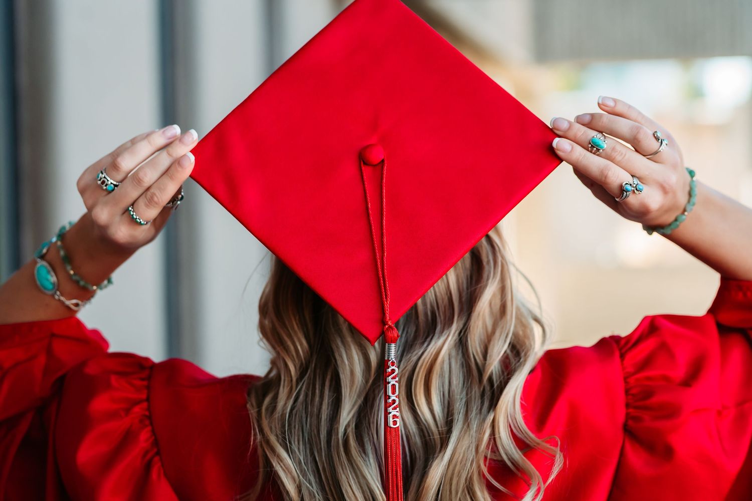 Graduate in bright red cap and gown smiling and holding diploma during outdoor graduation ceremony.