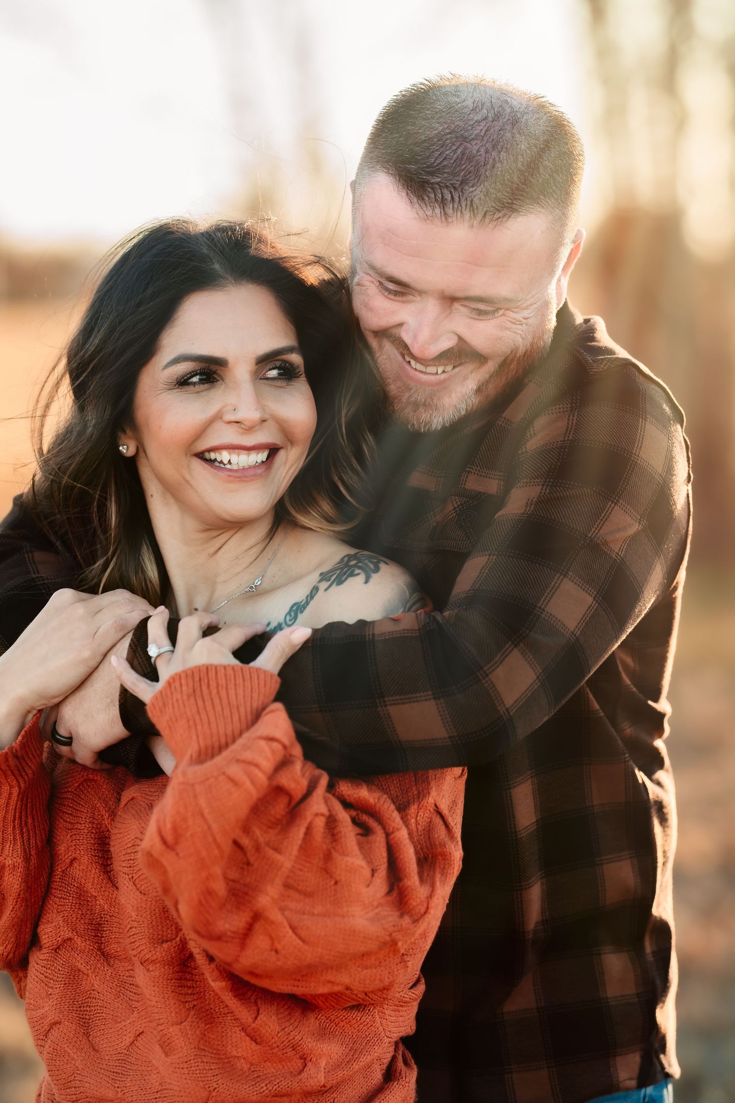 A couple shares intimate moments outdoors wearing autumn clothing with a warm orange sweater and plaid shirt.