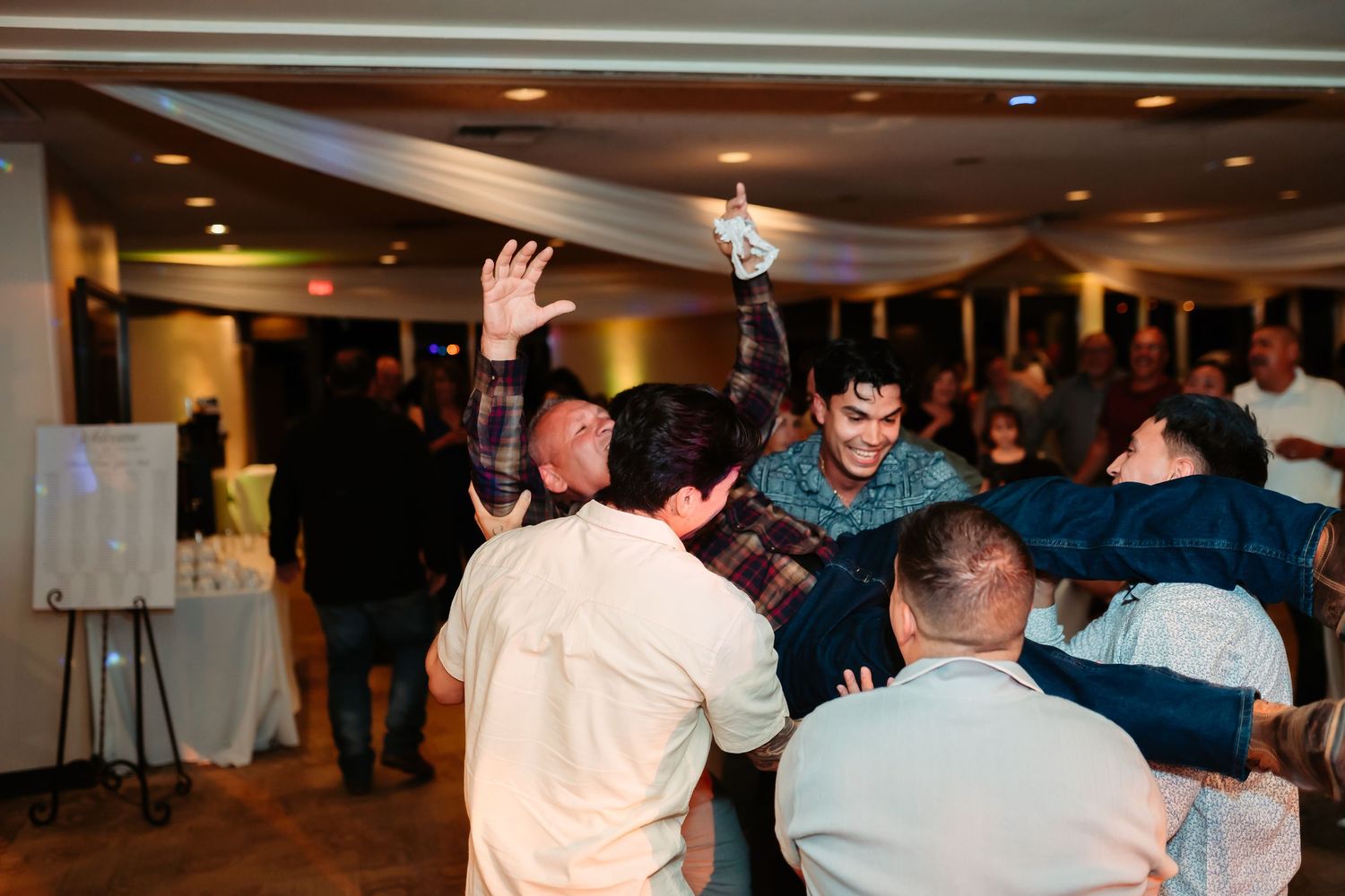 Wedding guests dancing and enjoying themselves on a lively reception dance floor under indoor lighting.