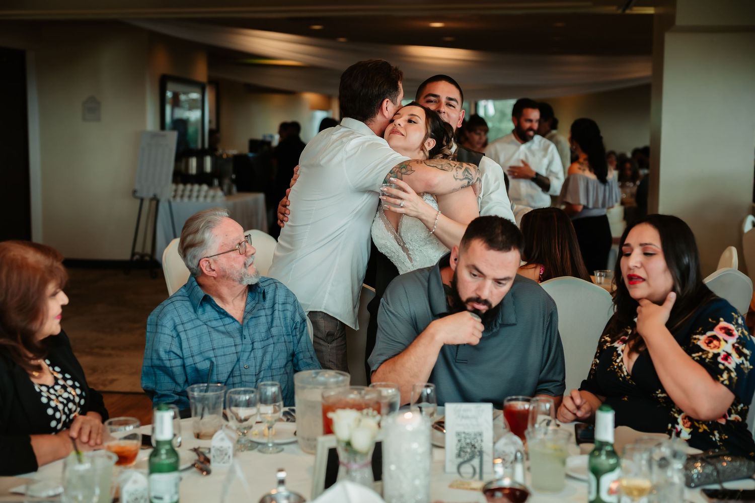 People dining together at long tables share conversation and laughter during a social gathering at an indoor venue.