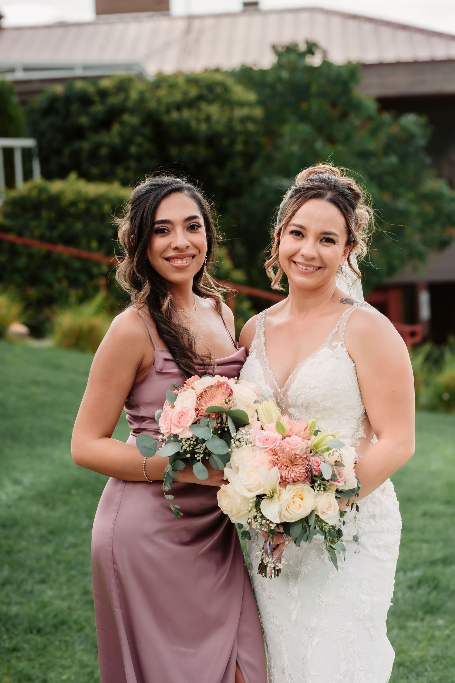 Bridesmaids in dusty rose dresses pose with bouquets of pink and white flowers on a grassy lawn.