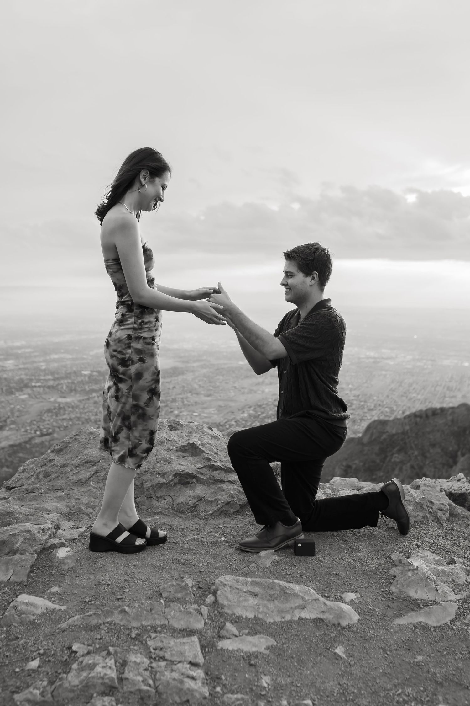 A proposal moment captured in black and white on a rocky mountain overlook.