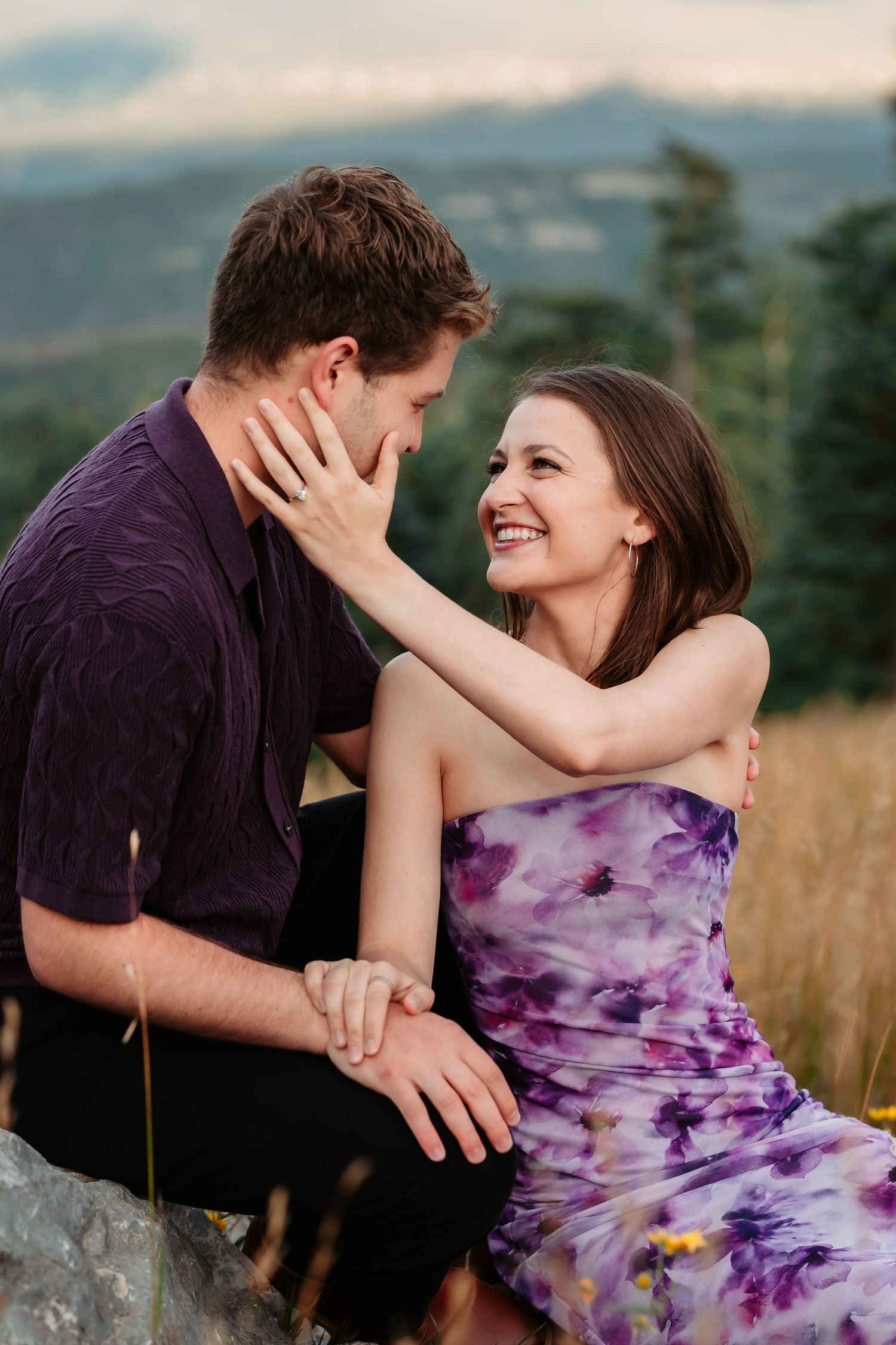 Loving couple sharing playful moments in purple outfits during golden hour mountain photoshoot.