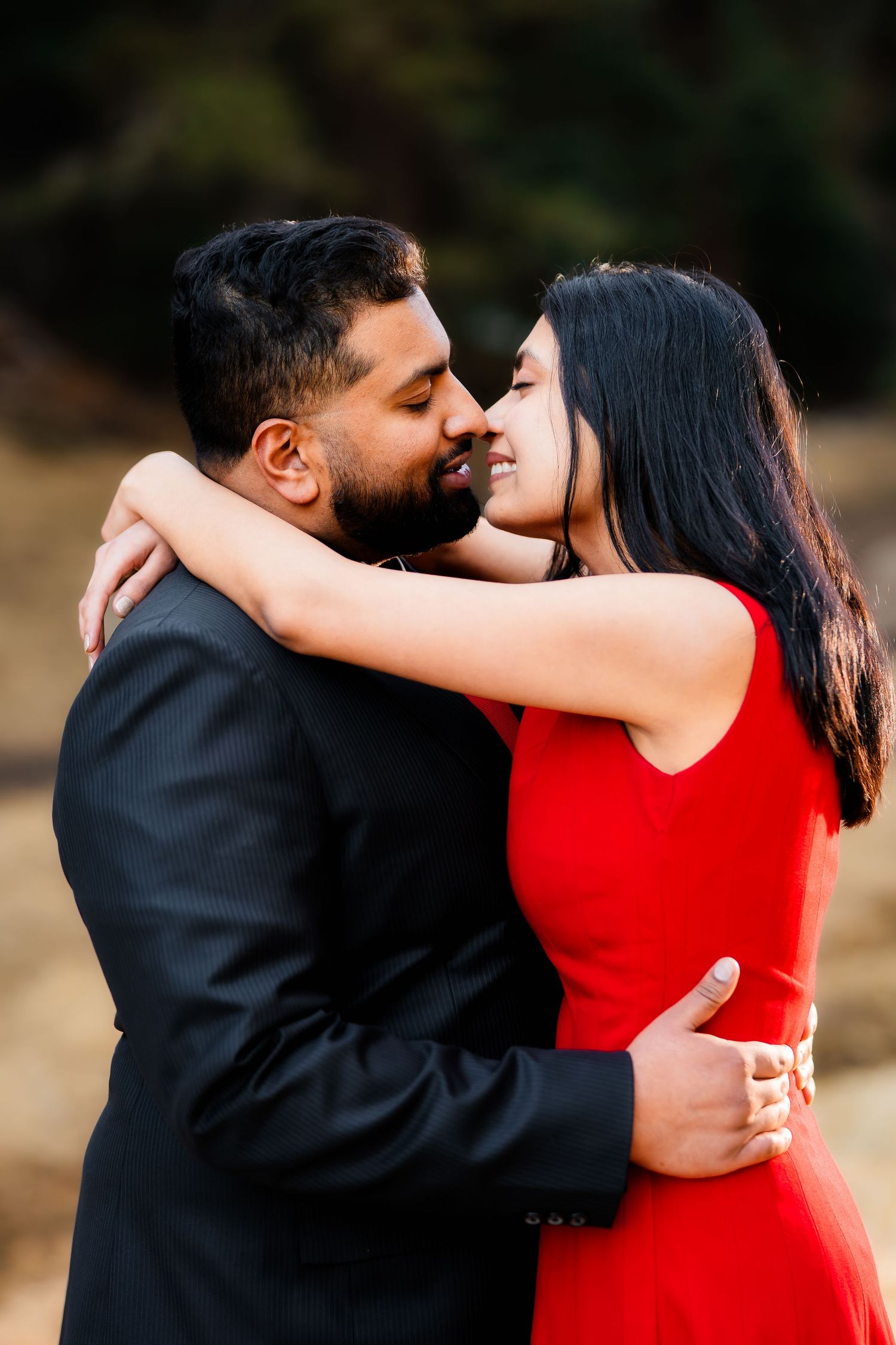 An intimate moment between a couple embracing, with the woman in a red dress against a natural backdrop.