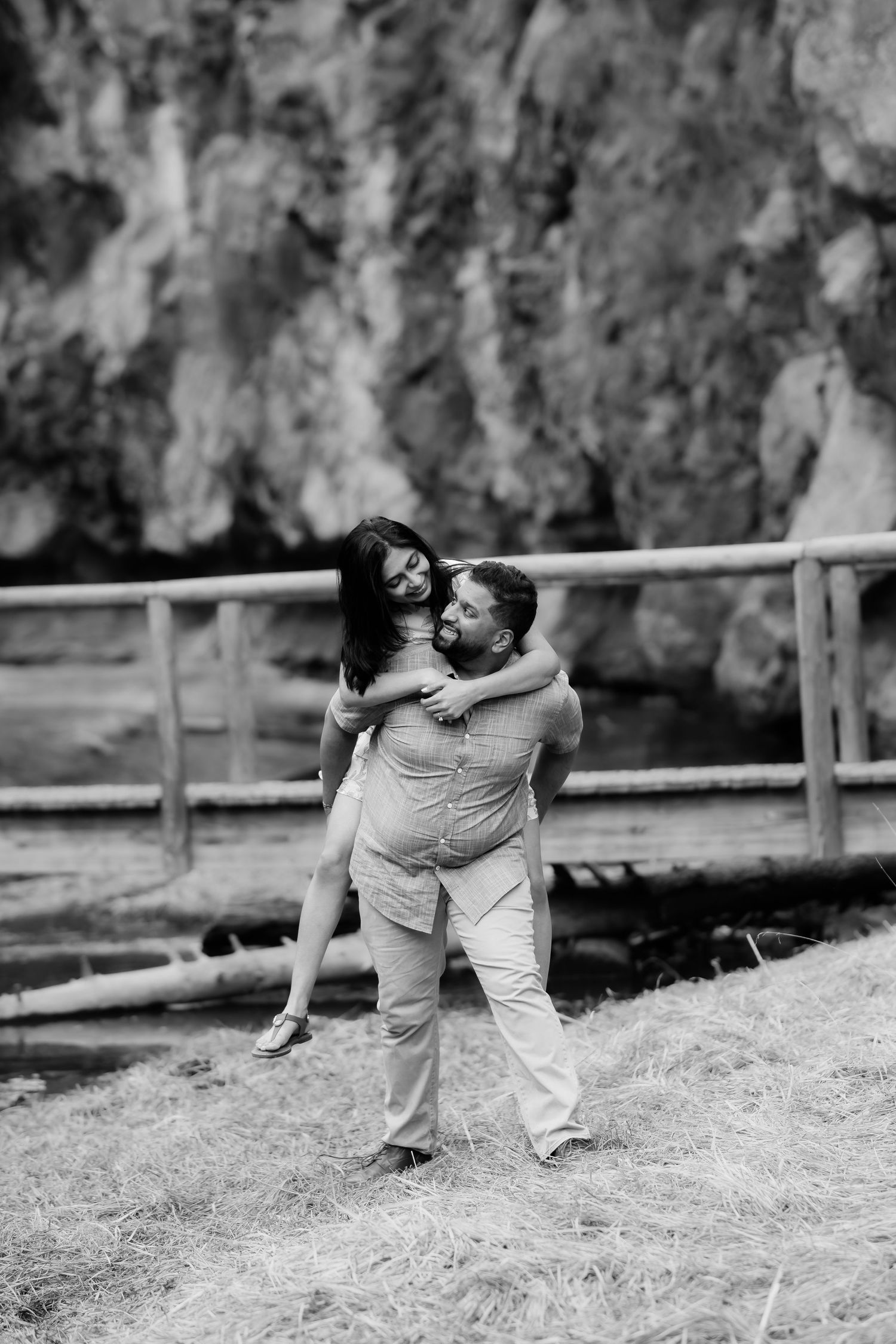 Playful couple sharing a candid moment by a rocky cliff face on a sunny afternoon.