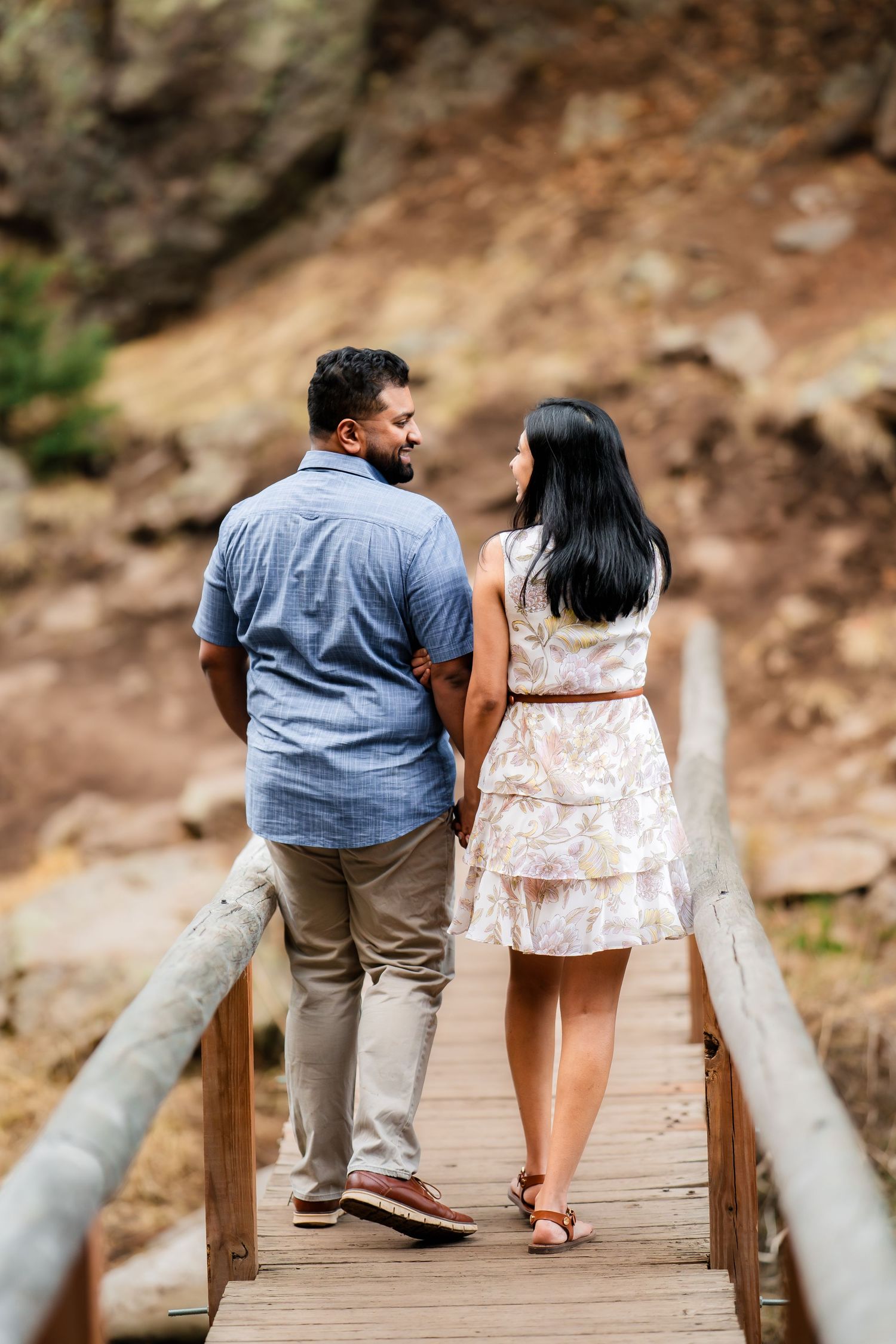 A couple walks together on a wooden boardwalk against a rocky natural backdrop.