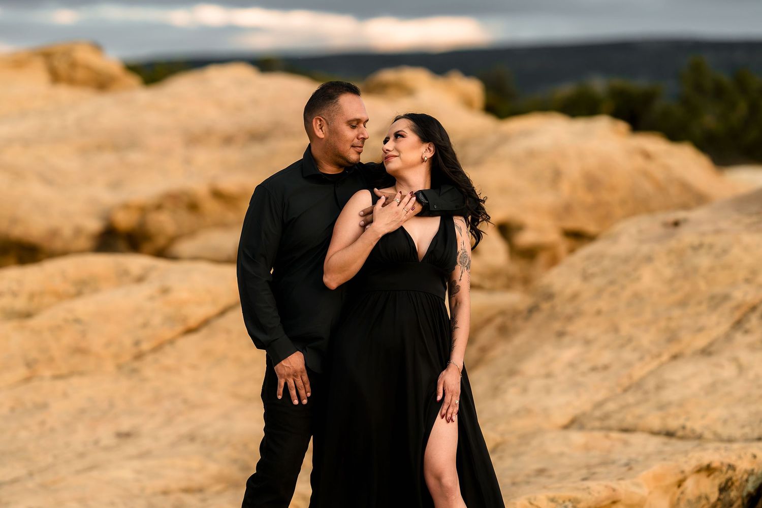 Intimate couple in matching black outfits sharing a tender moment against golden desert rock formations.