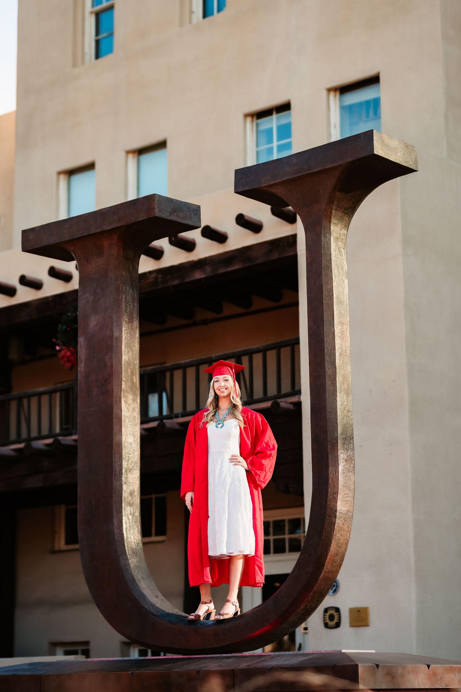 A person in a bright red cardigan and white dress poses in a series of architectural frames at a building entrance.