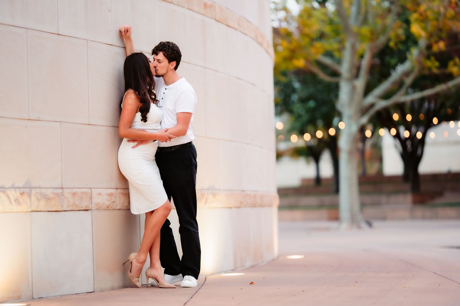 A couple shares a romantic moment among white stone columns at sunset in an outdoor setting.