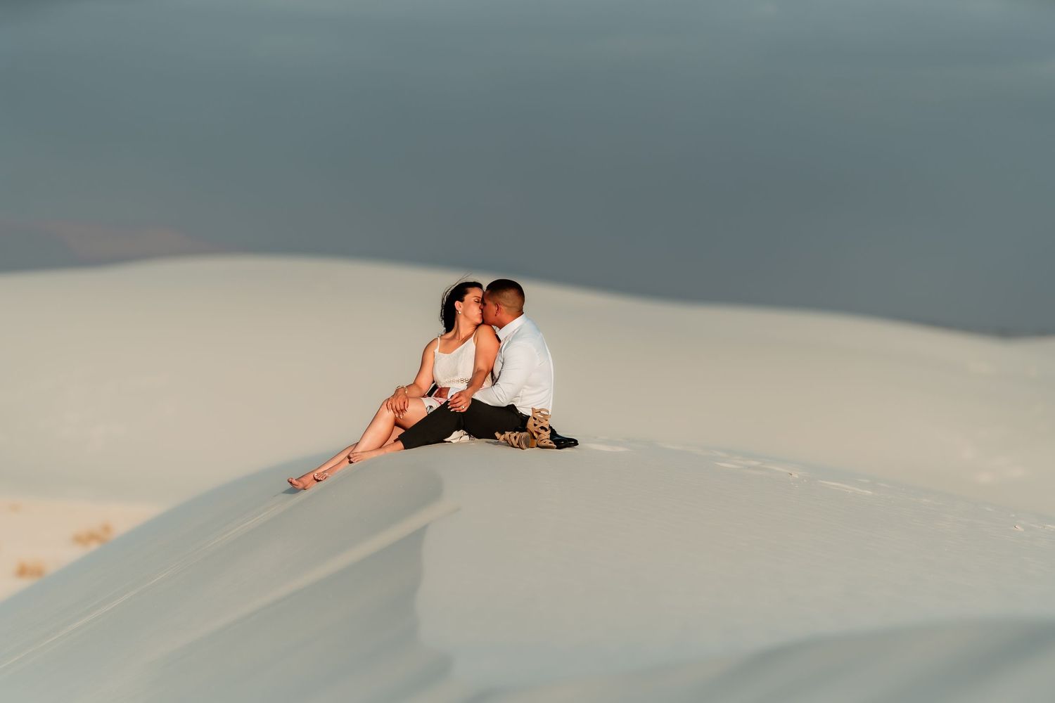 Two people lie on white sand dunes at sunset creating dramatic shadows and silhouettes against the sky.