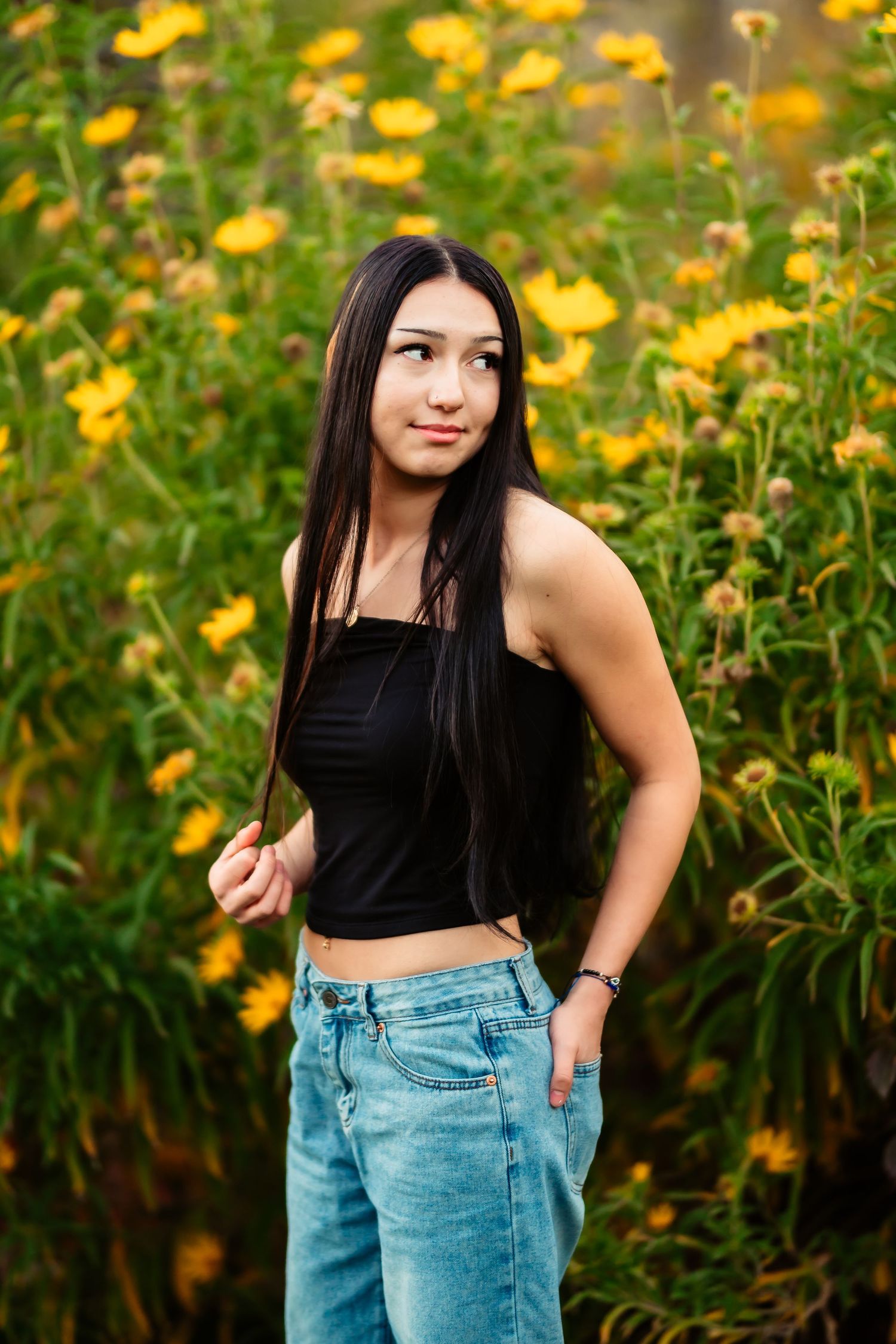 Portrait in a garden with vibrant yellow flowers, wearing casual denim and a black top.