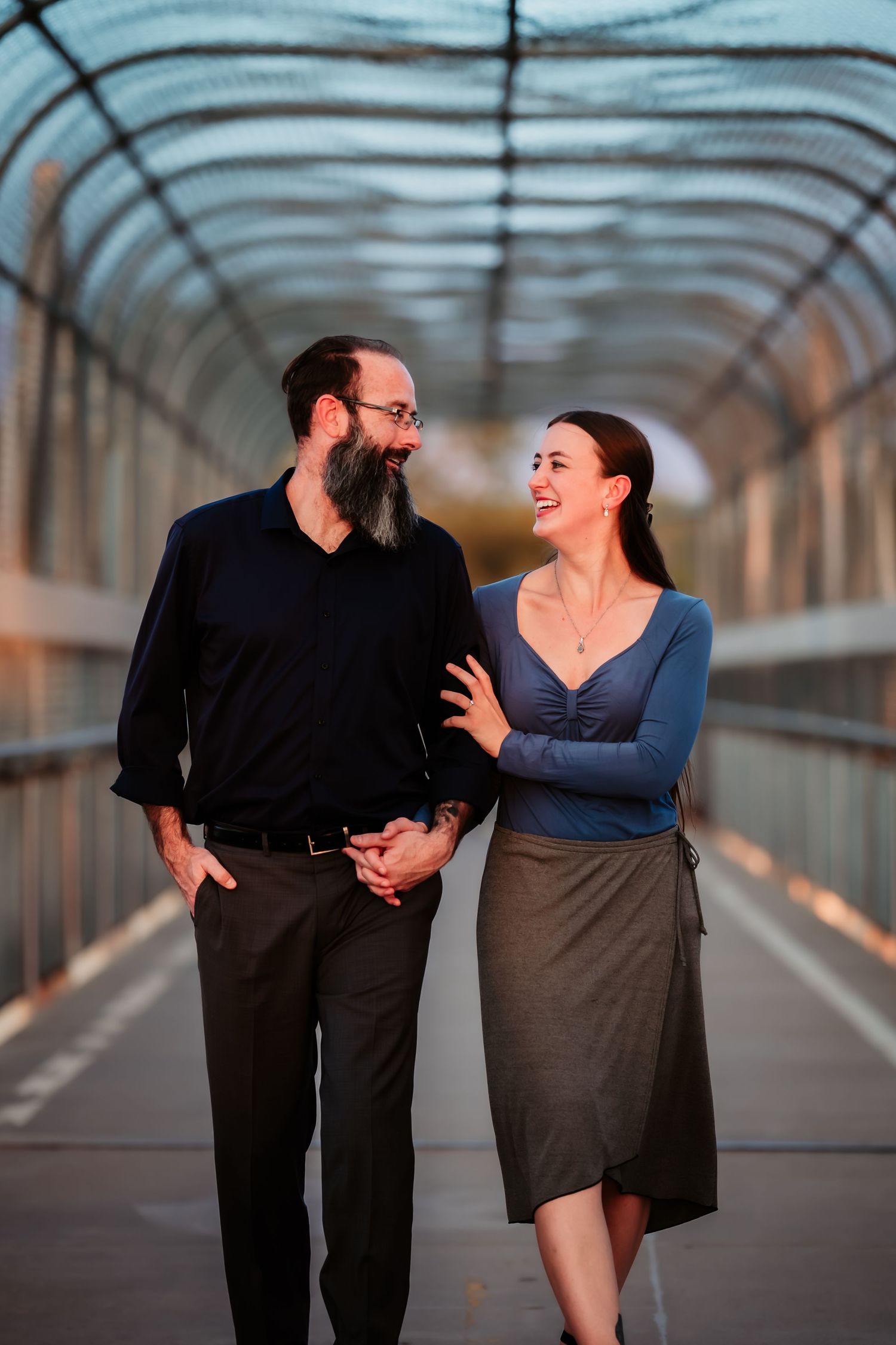 A couple shares a romantic moment while walking together on a covered bridge at sunset.