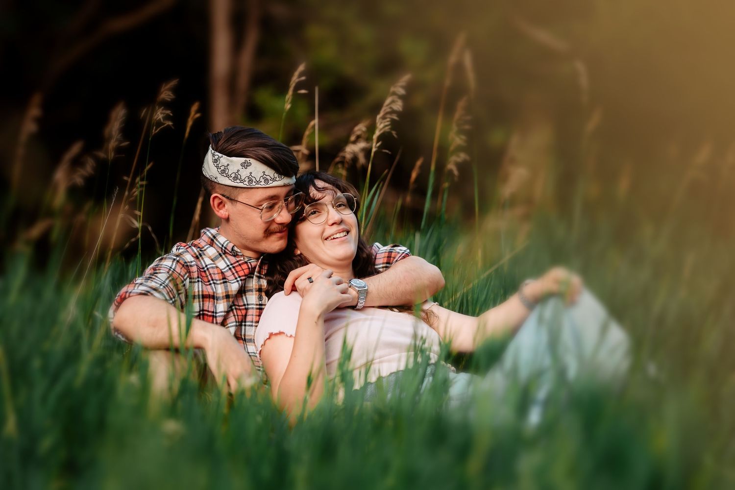A romantic couple relaxes in tall grass during a summer outdoor photoshoot.