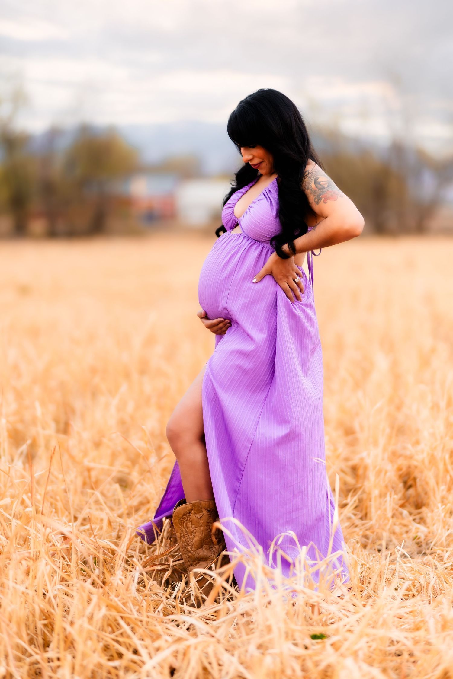 A figure in a flowing purple dress crouches gracefully in a golden wheat field during sunset.