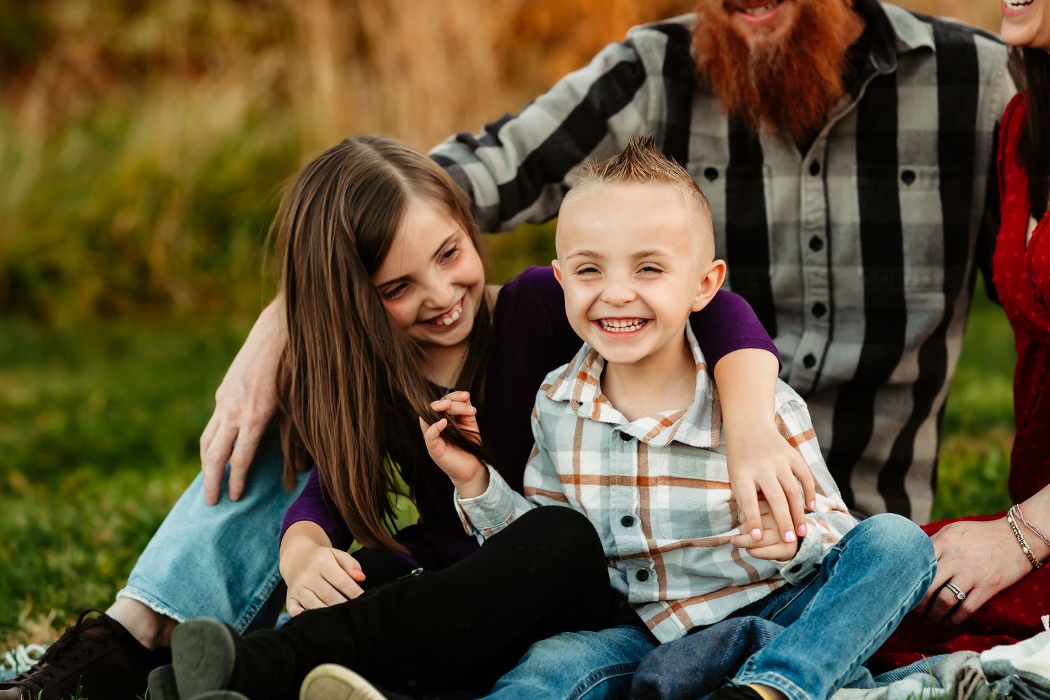Family enjoying playful moments together while sitting in autumn grass during outdoor photo session.