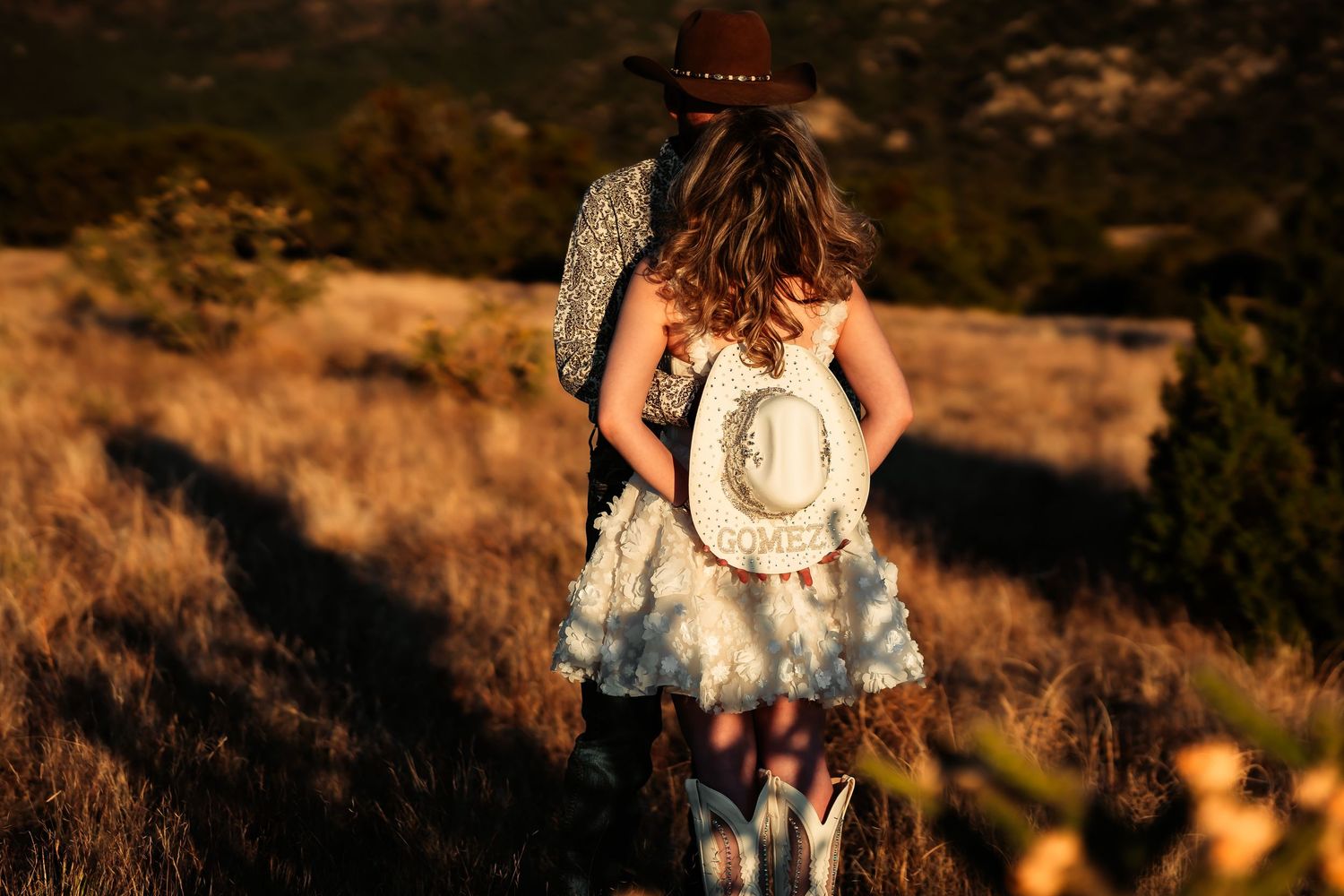 A person in a floral dress stands in golden sunlight on a hillside during sunset.