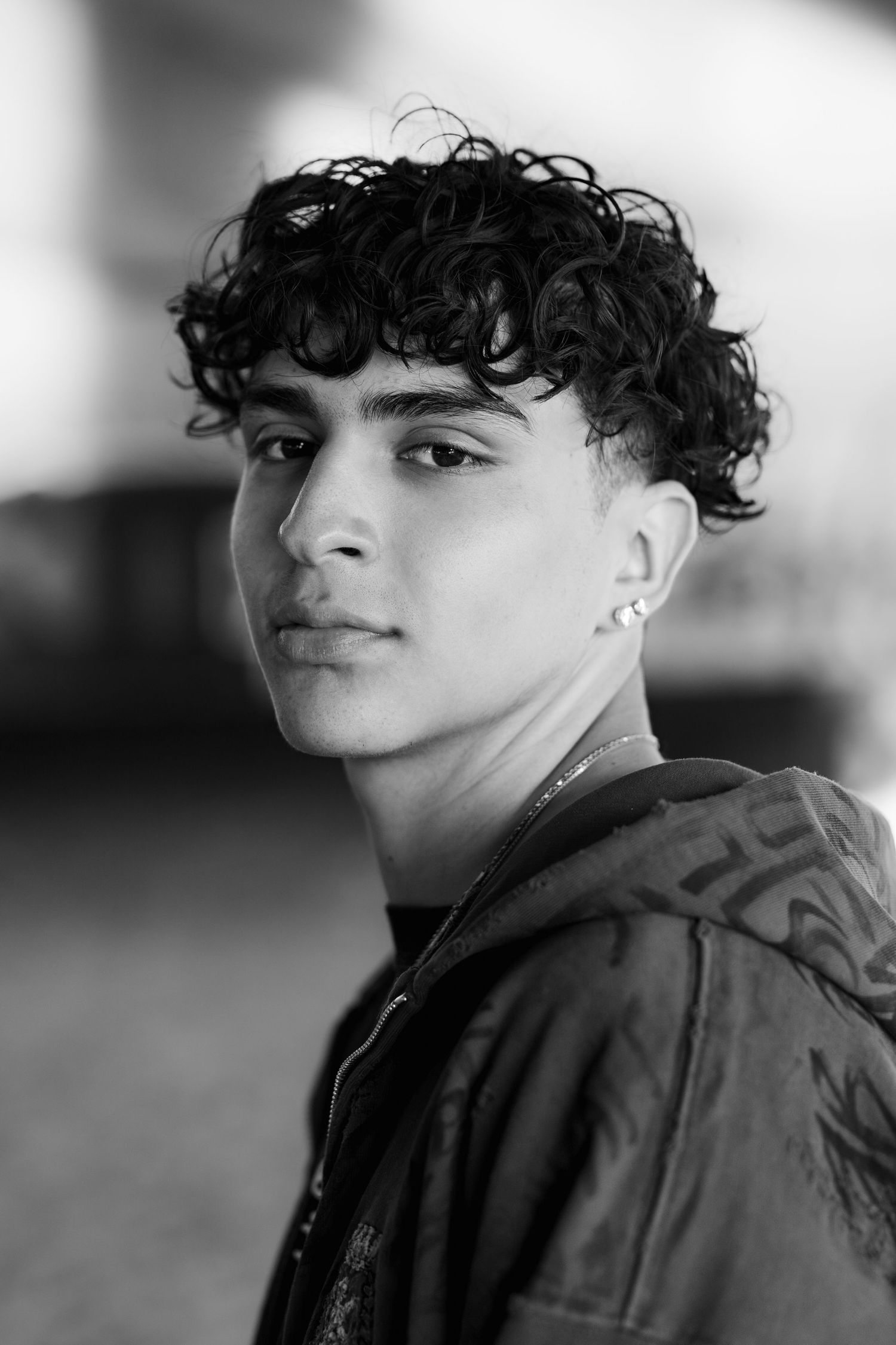 Black and white portrait shot of young individual with curly hair and earring wearing a dark jacket.