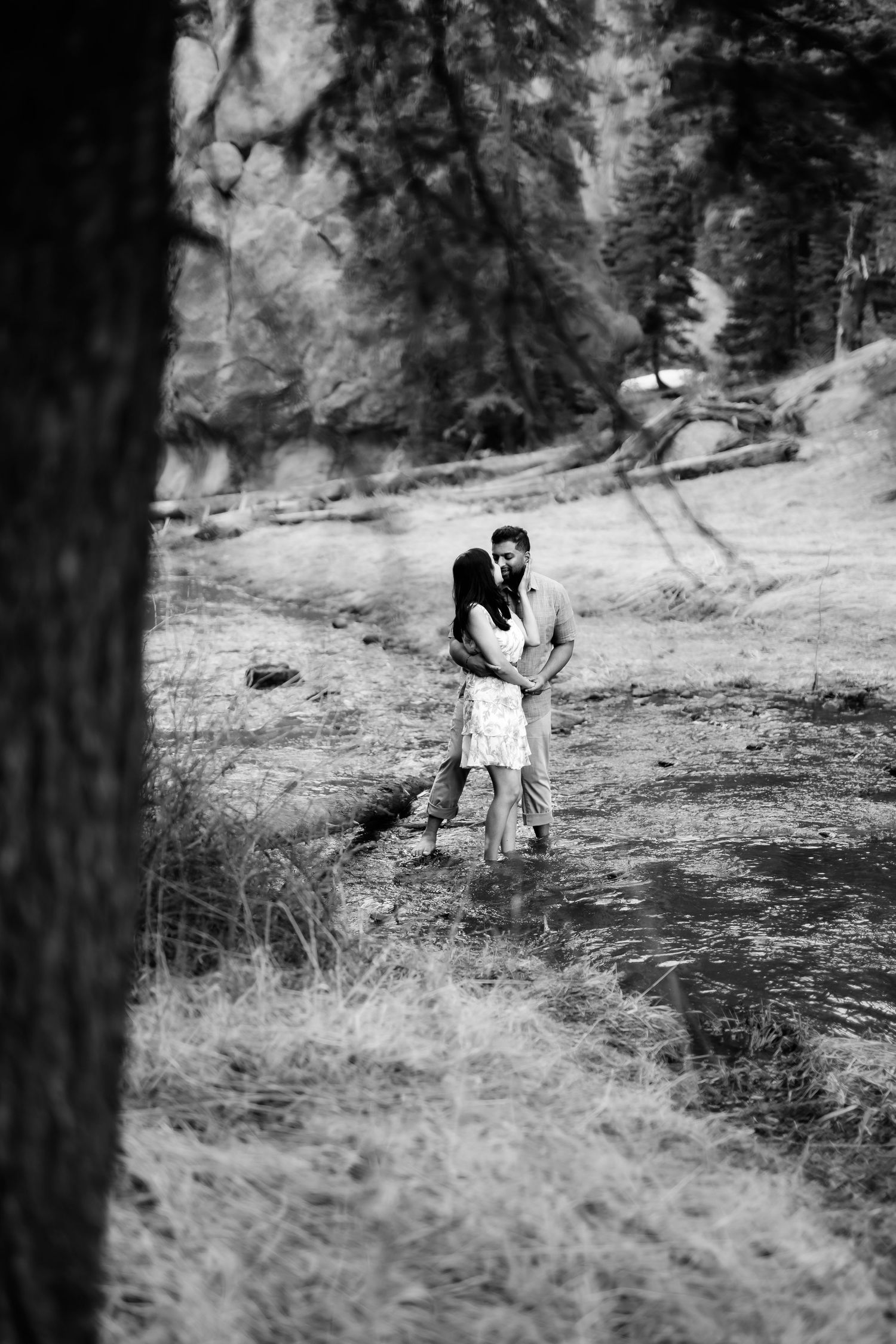 A romantic black and white photo of a couple embracing in a wooded mountain setting.