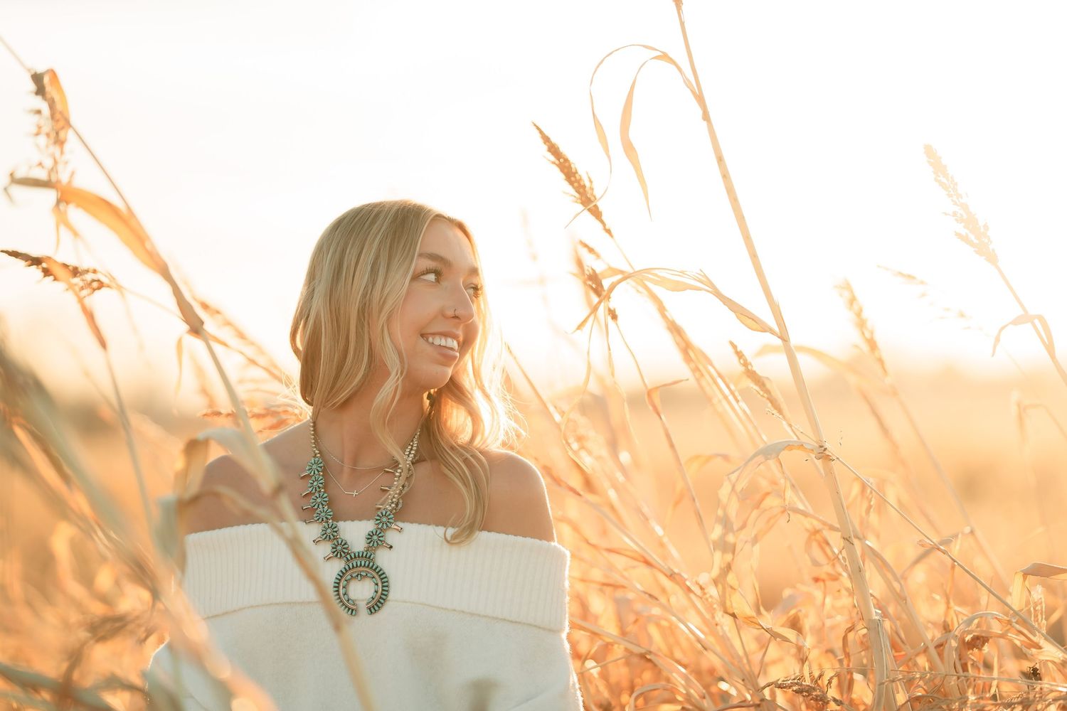 Person in a white off-shoulder dress standing in a golden wheat field at sunset with warm glowing light.