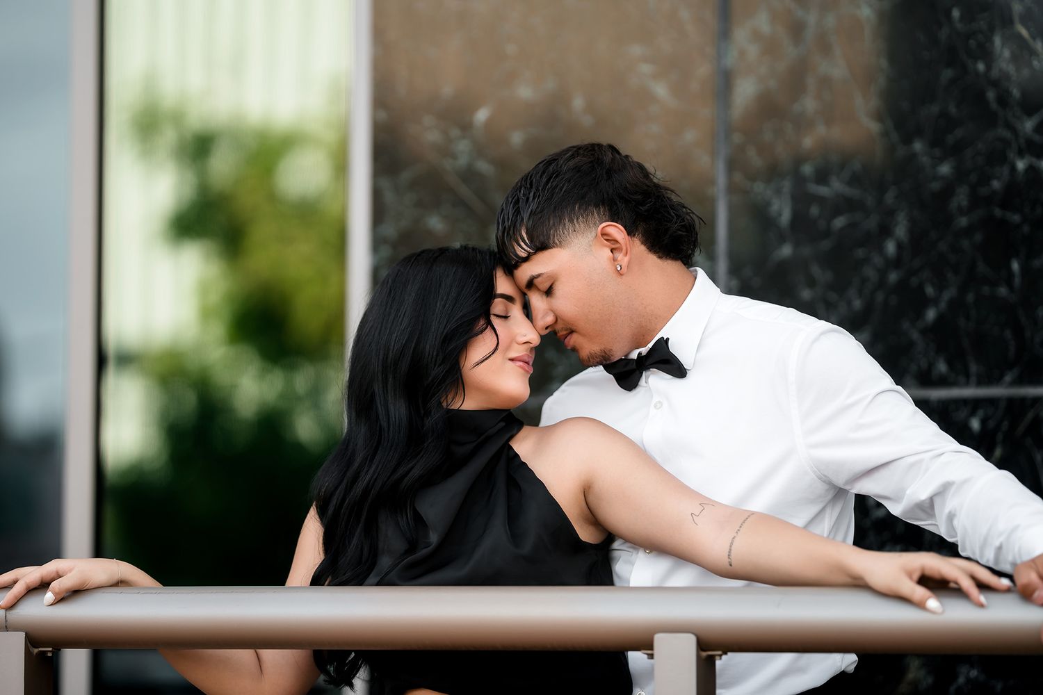 Romantic couple in formal attire sharing a tender moment, man in tuxedo leaning in to kiss smiling woman in black dress.