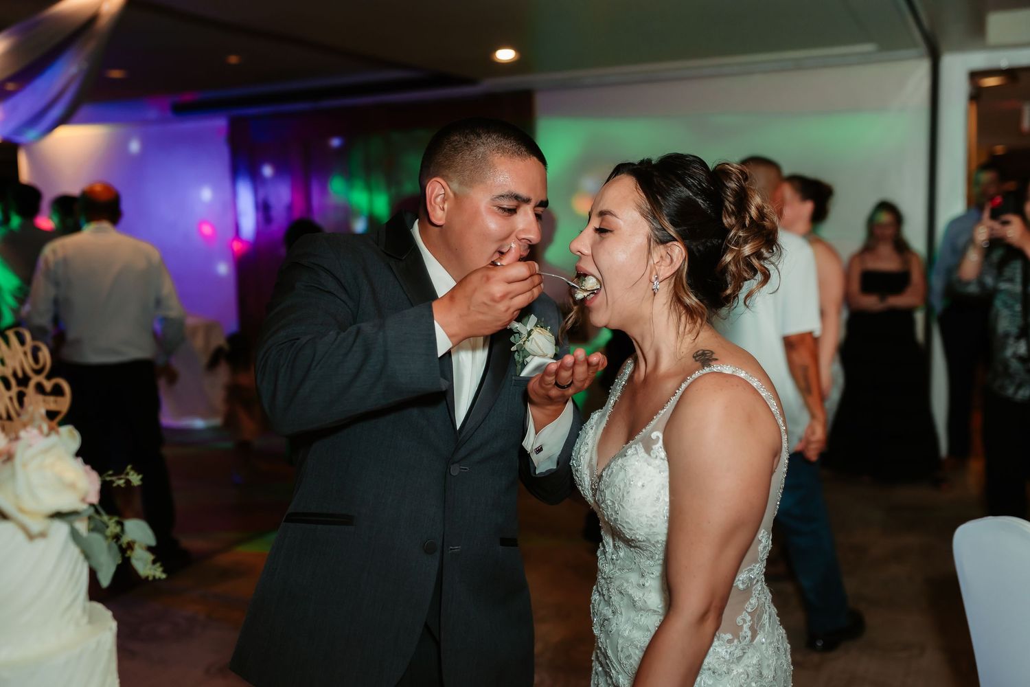 Newlyweds playfully feed each other wedding cake during their reception.